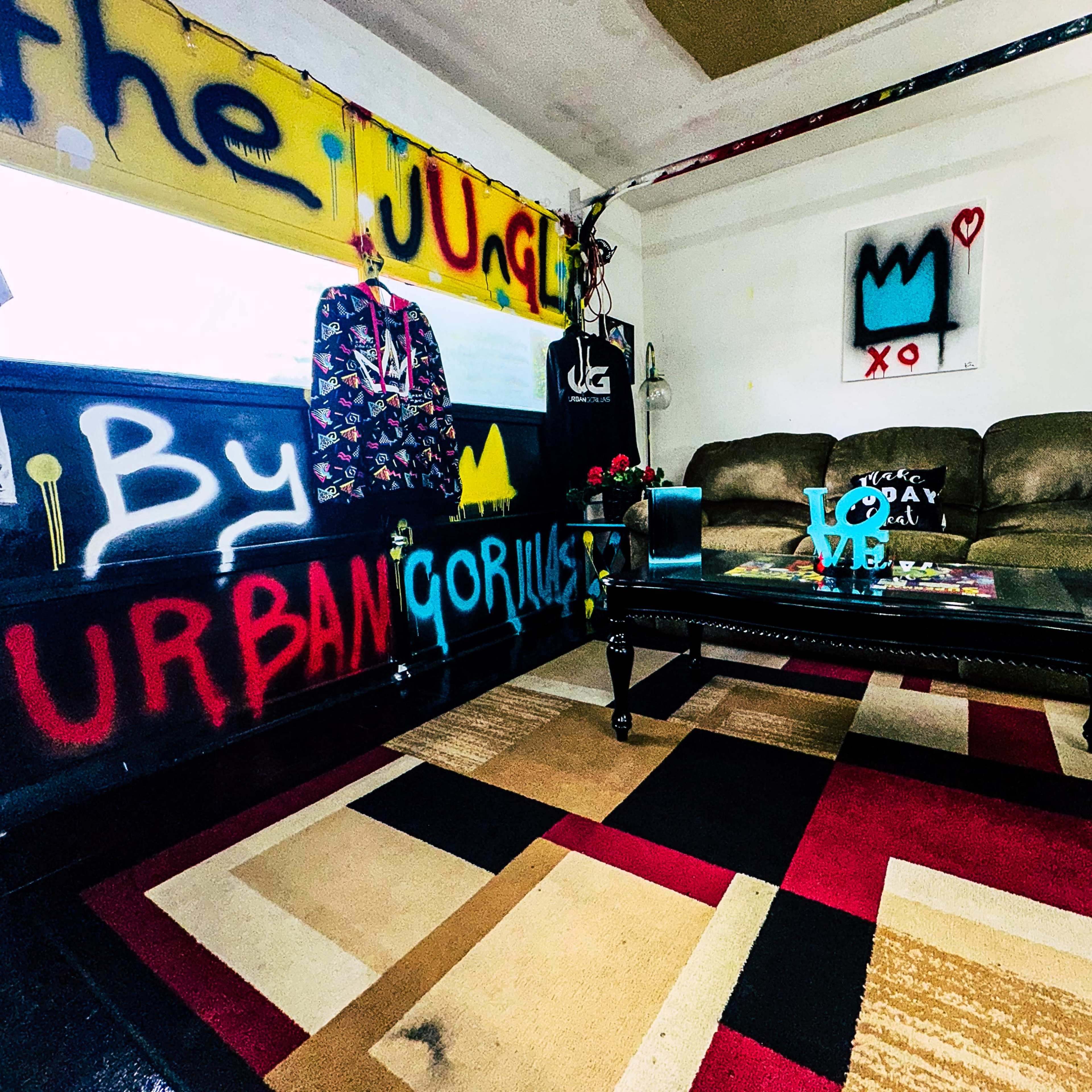 A creatively decorated room featuring graffiti on the walls, a brown sofa, and a coffee table on a multicolored rug.