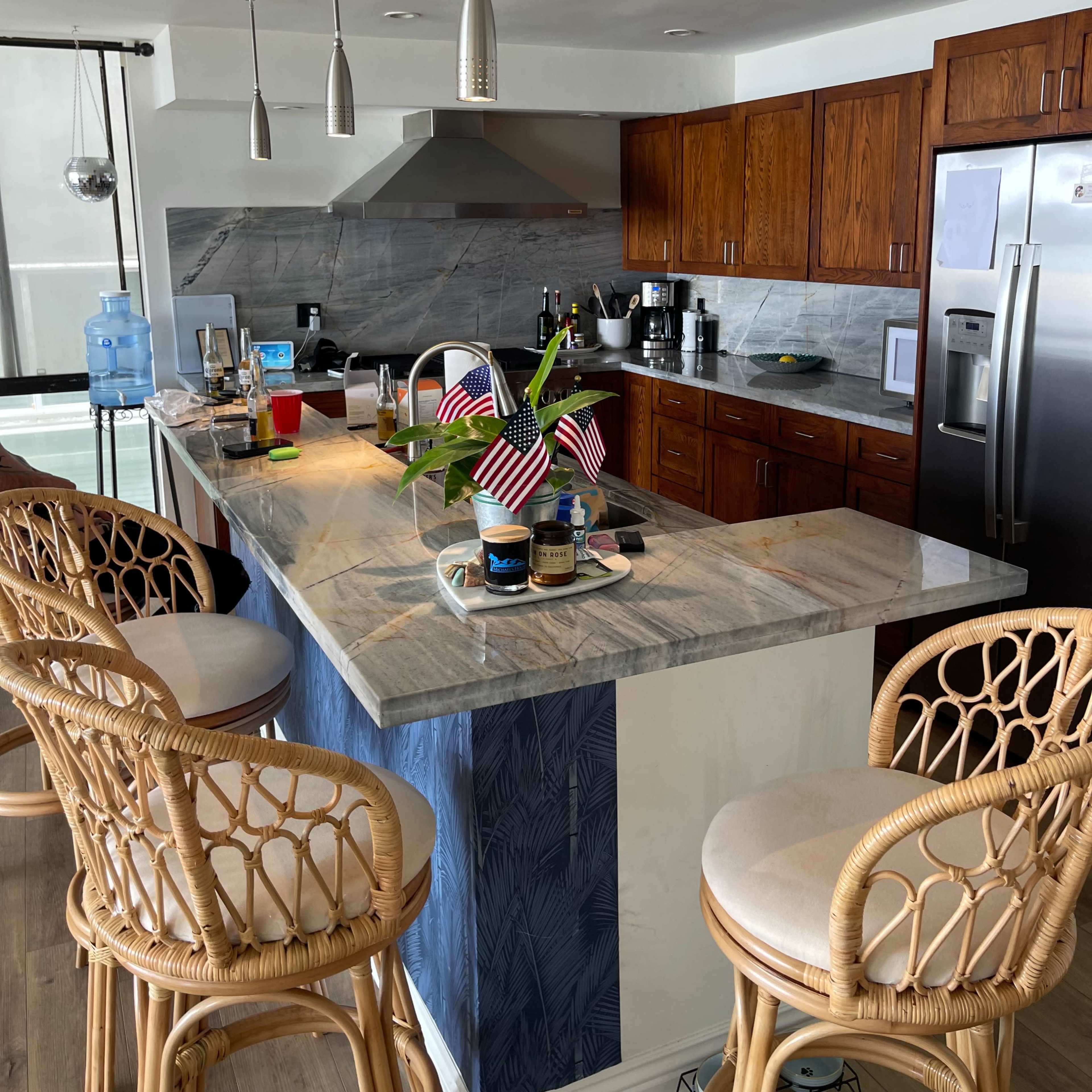 A modern kitchen with a marble island, wooden cabinets, and bar stools, featuring decorations and various kitchen items on the counter.