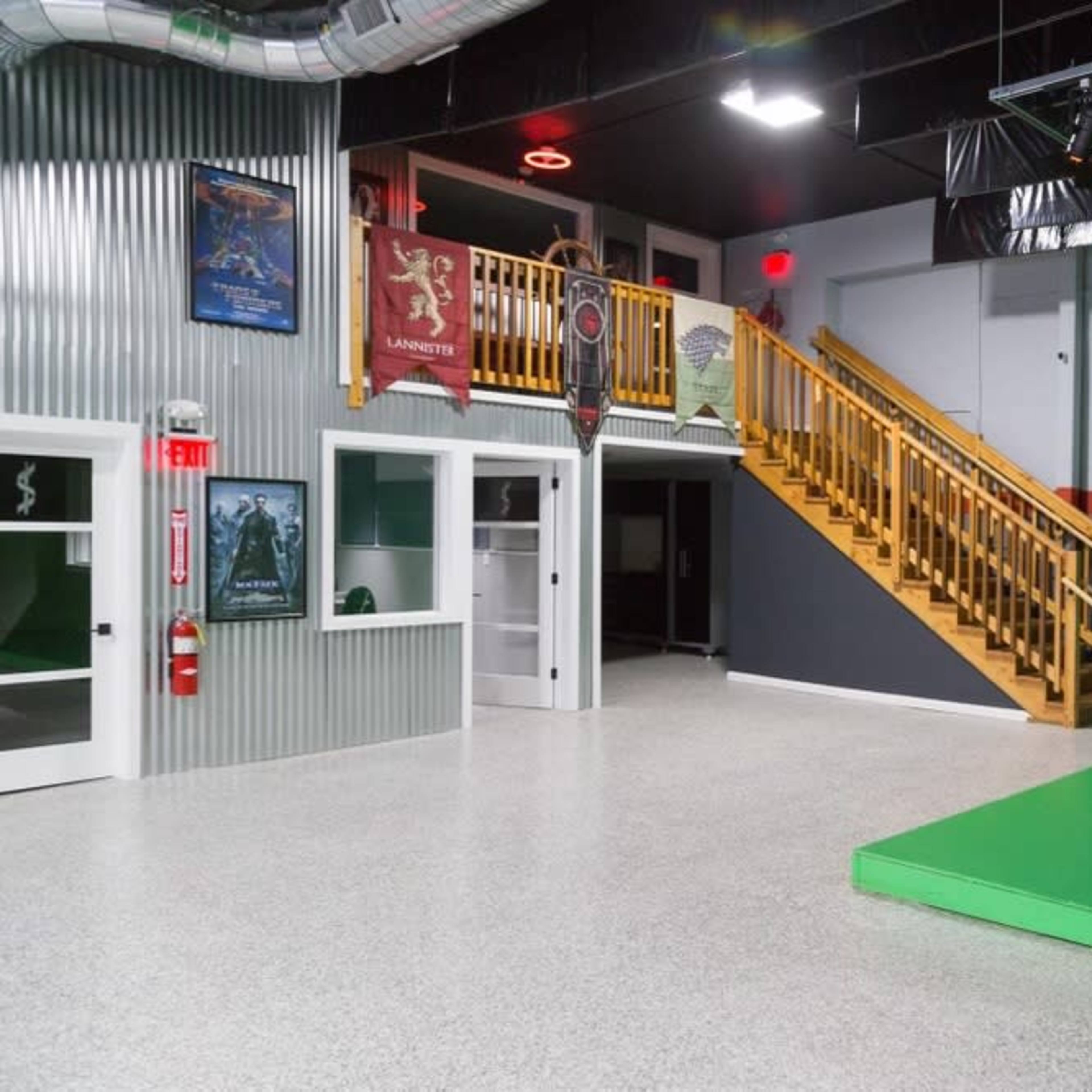 A spacious film studio with a green screen area, a staircase leading to an upper level, and various posters on the walls.