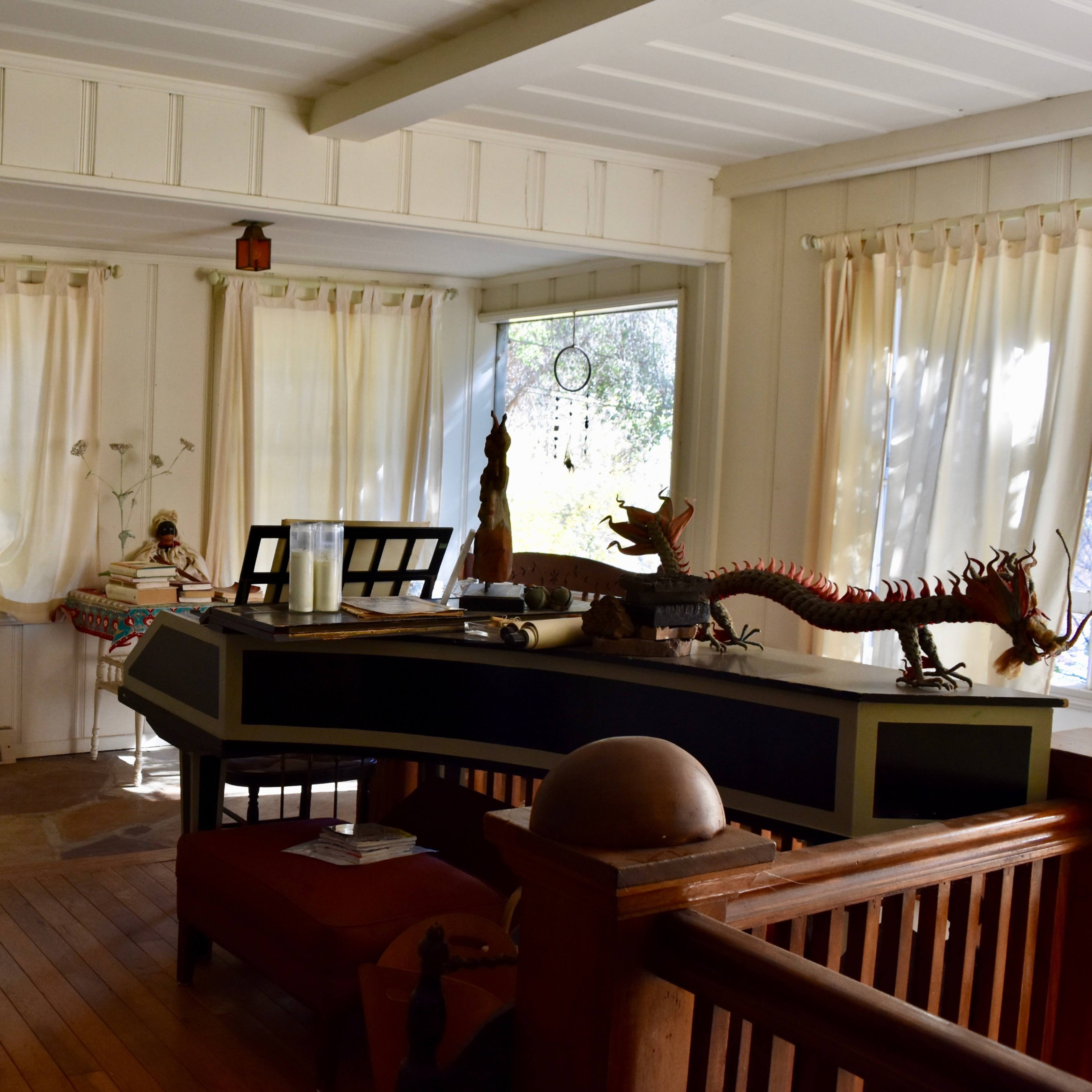 A bright, airy interior room with wooden flooring, large windows covered by sheer curtains, and various decorative items on a dark console table.