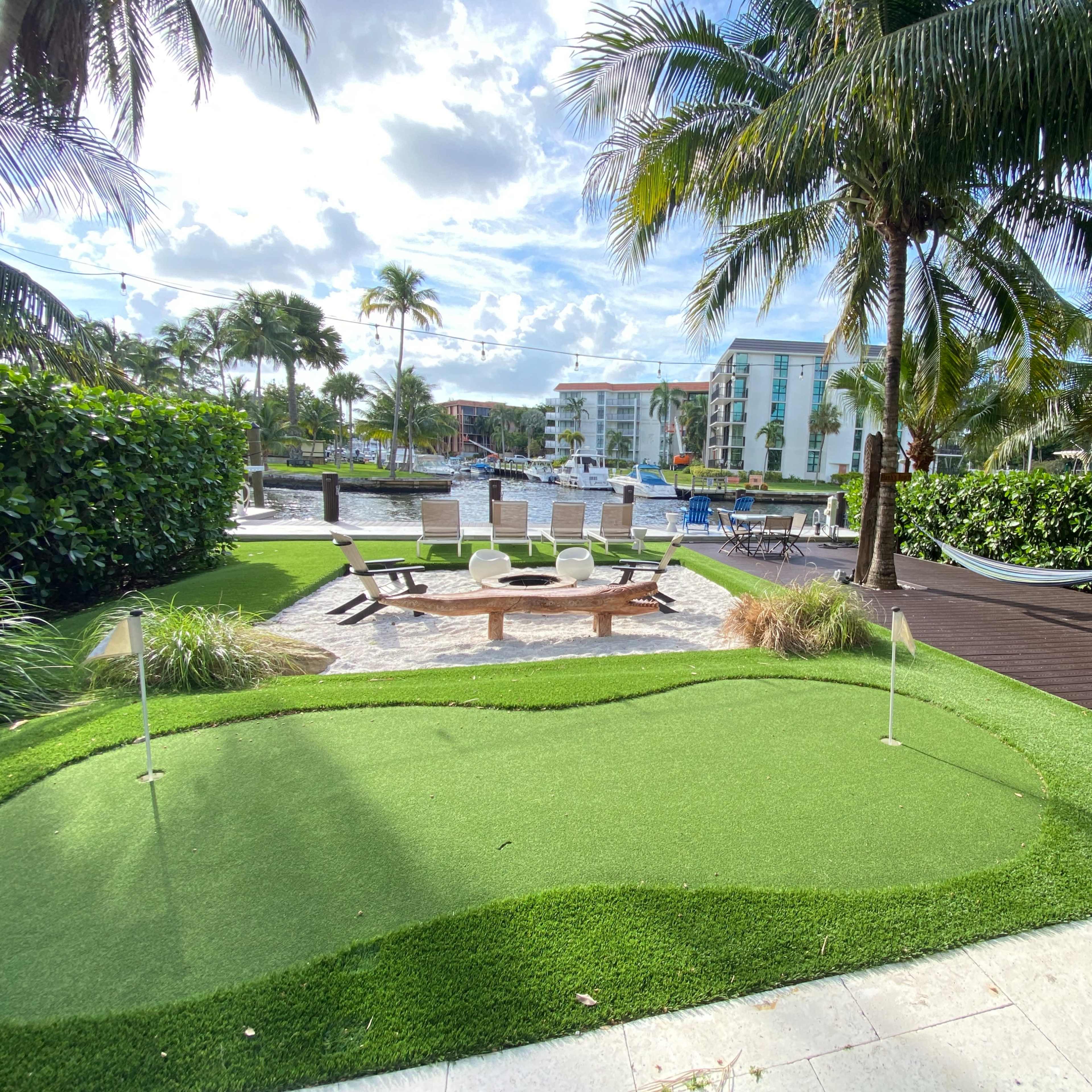 A mini-golf area with two flags, surrounded by palm trees and a seating area by a body of water.