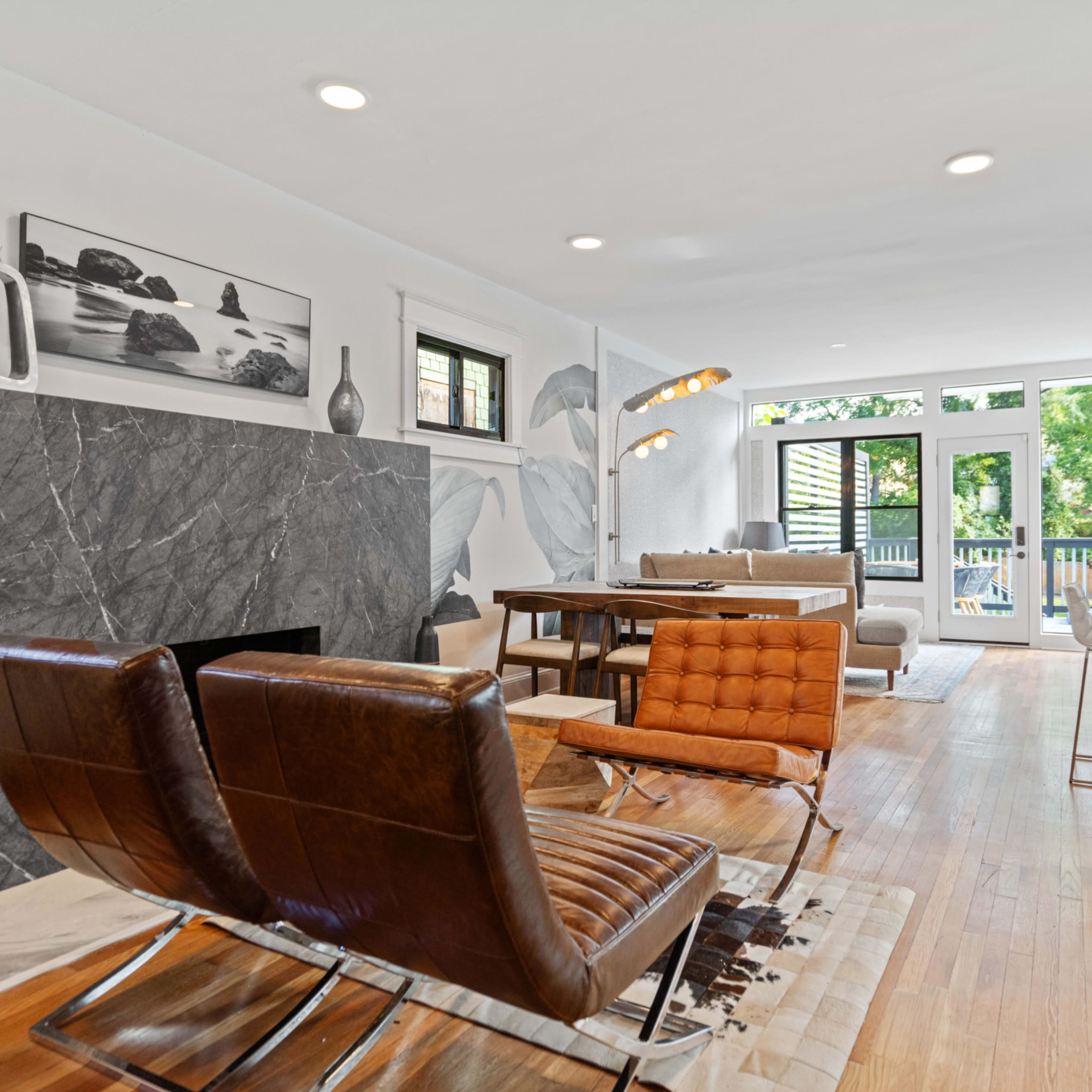 A modern living room with a marble fireplace, a dining table, and large windows leading to a balcony.