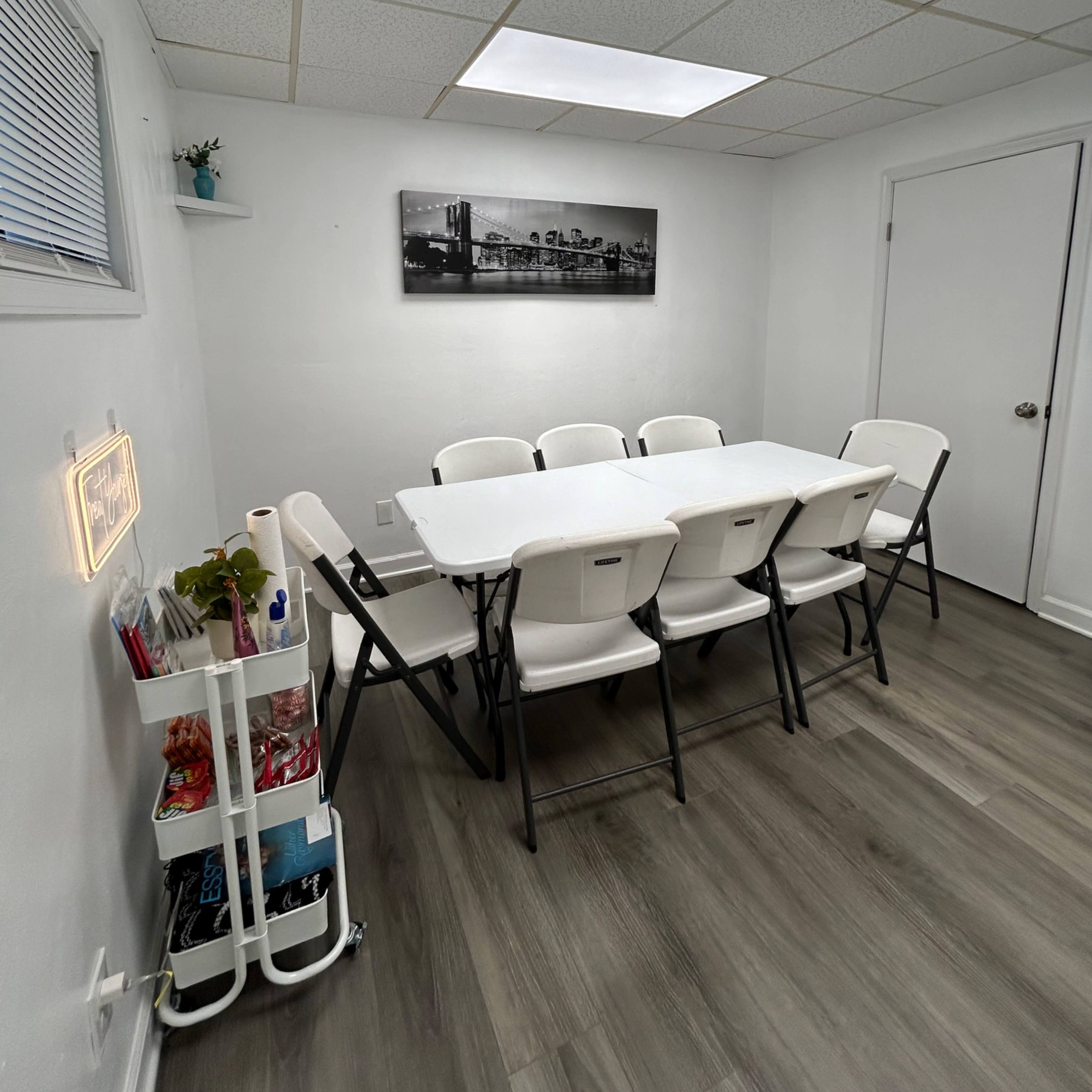 A conference room is set up with a long table surrounded by folding chairs under bright overhead lights.