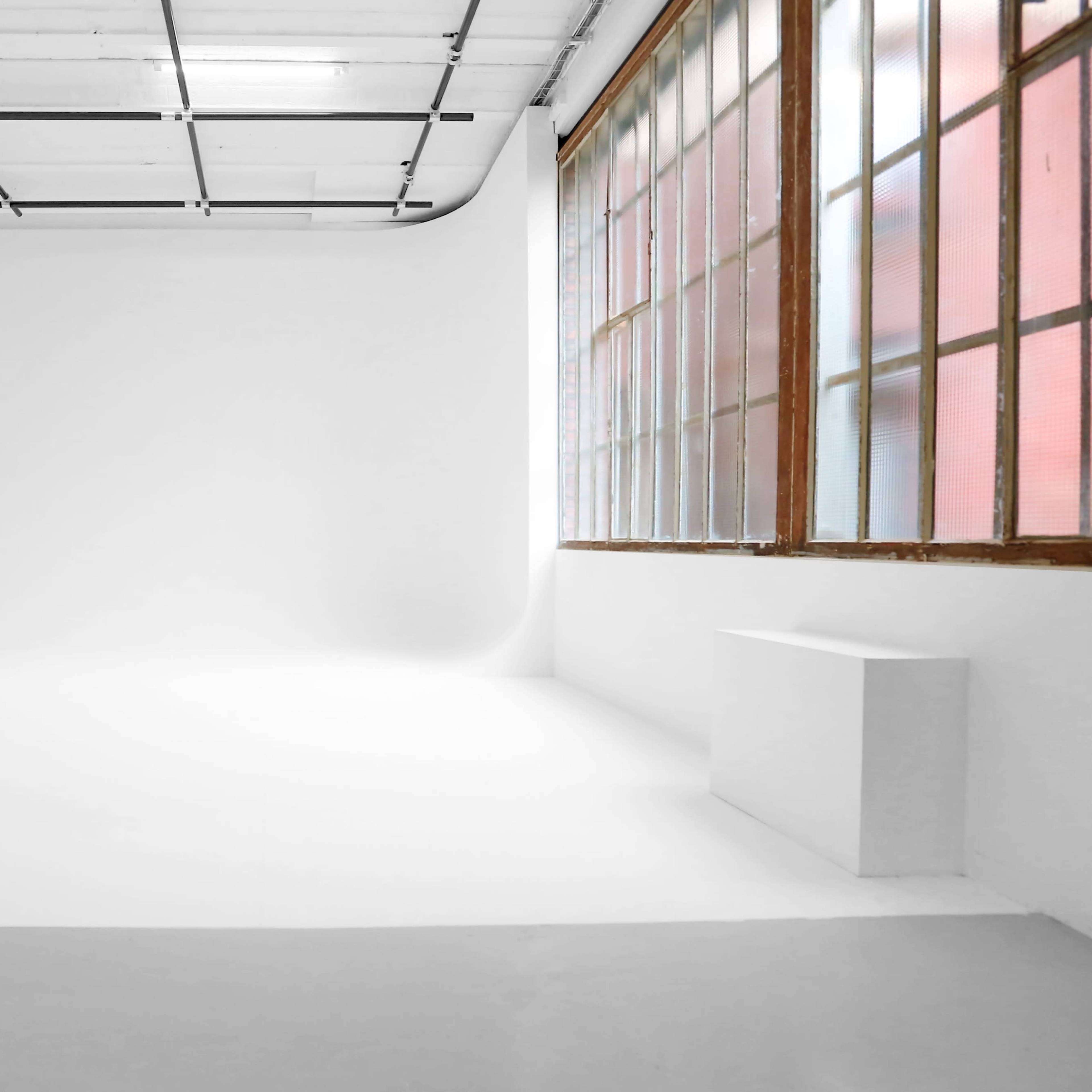 A bright, empty studio space features white walls, a smooth floor, and large windows allowing natural light.