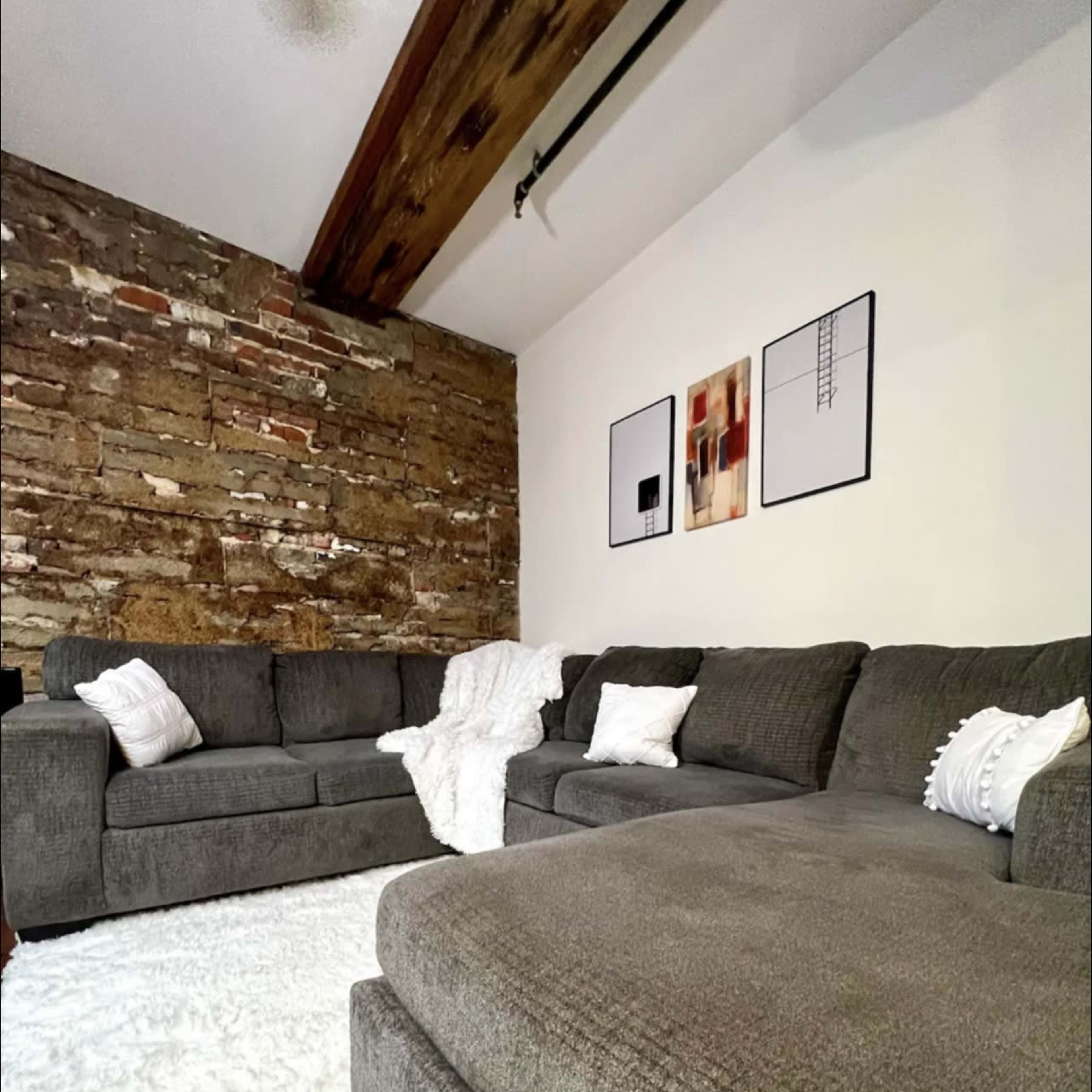A cozy living room features a sectional sofa and two armchairs placed on a plush rug against a rustic stone wall.
