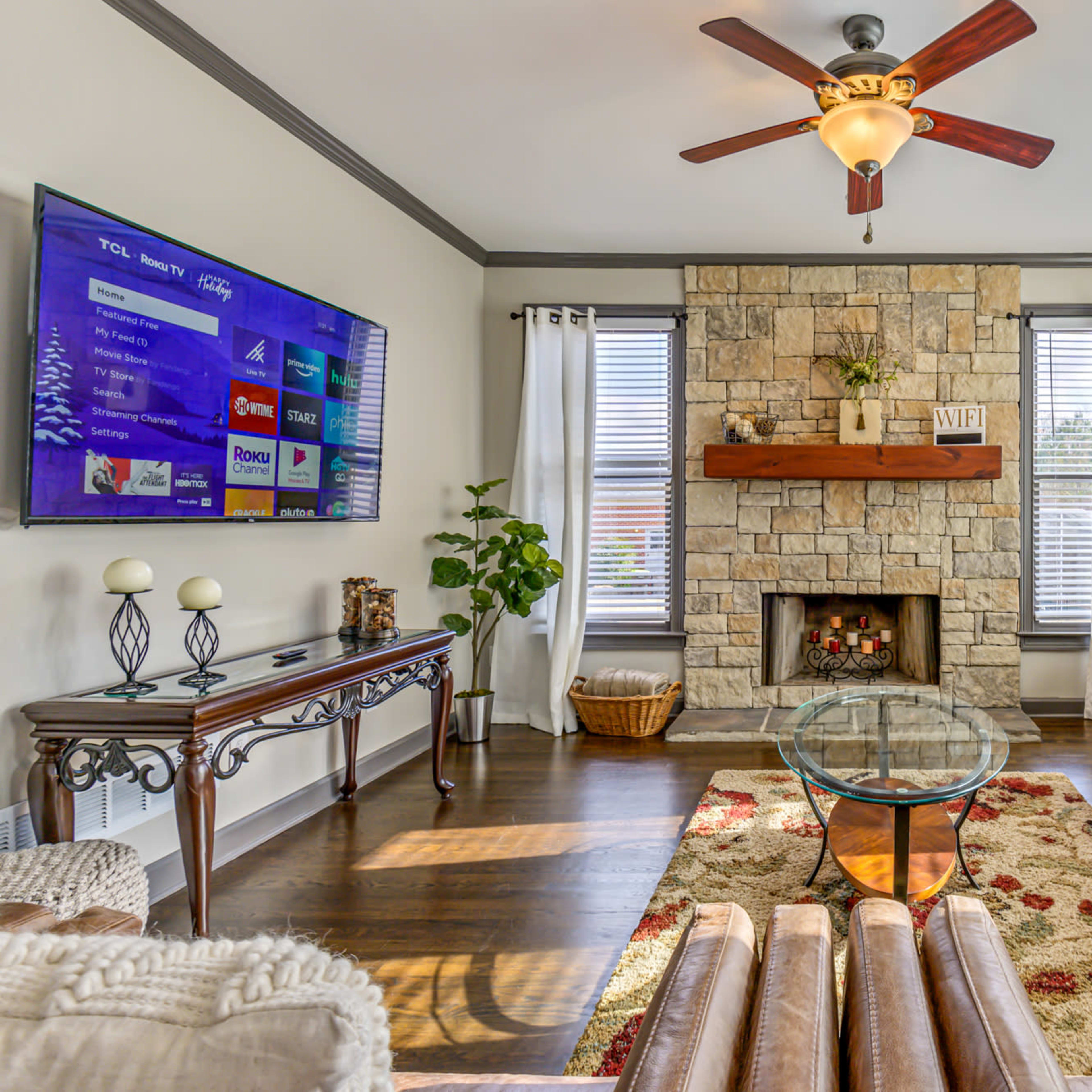 A cozy living room featuring a stone fireplace, a large television mounted on the wall, and comfortable seating arranged around a glass coffee table.