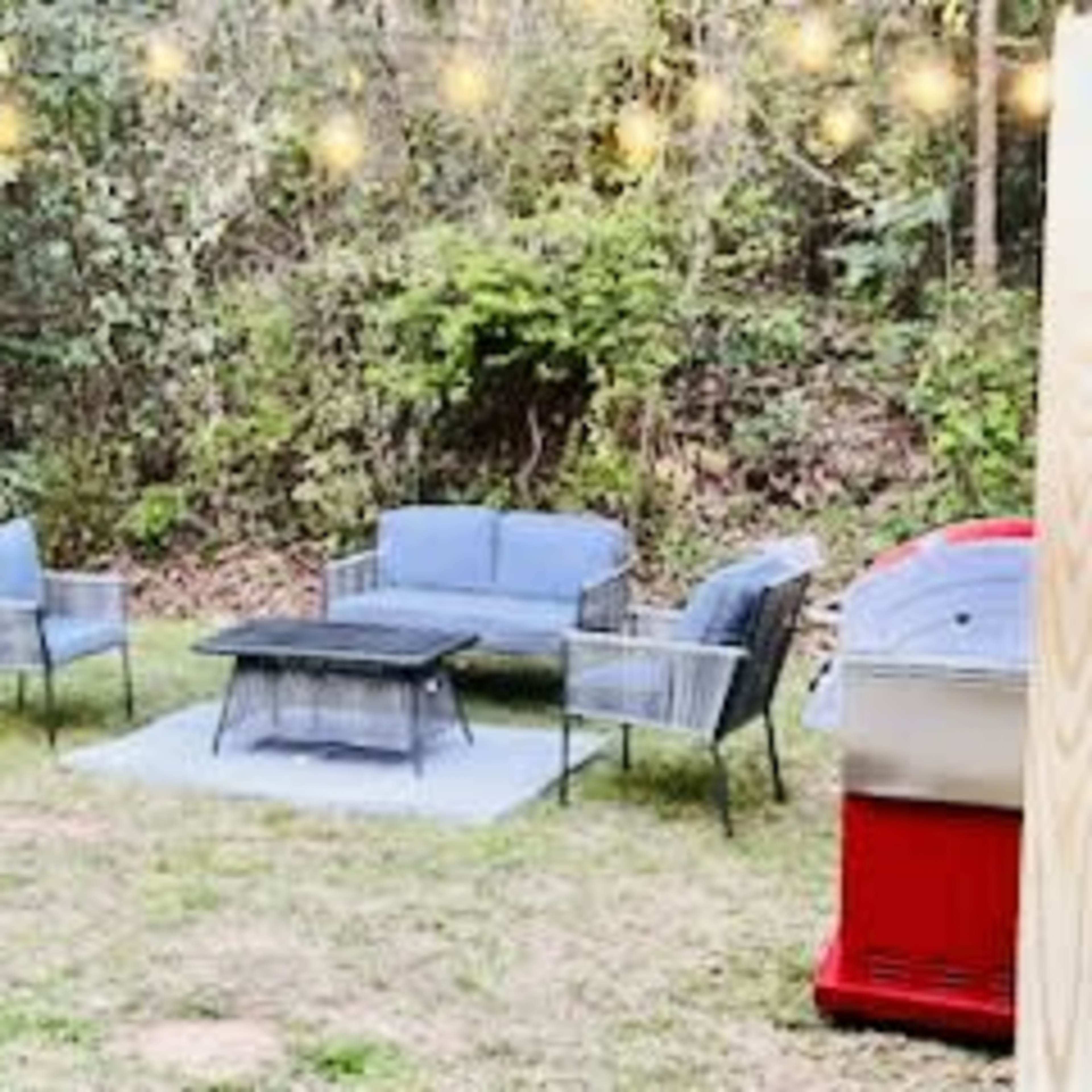 A seating area with four chairs and a coffee table is set up on grass under string lights in a backyard.