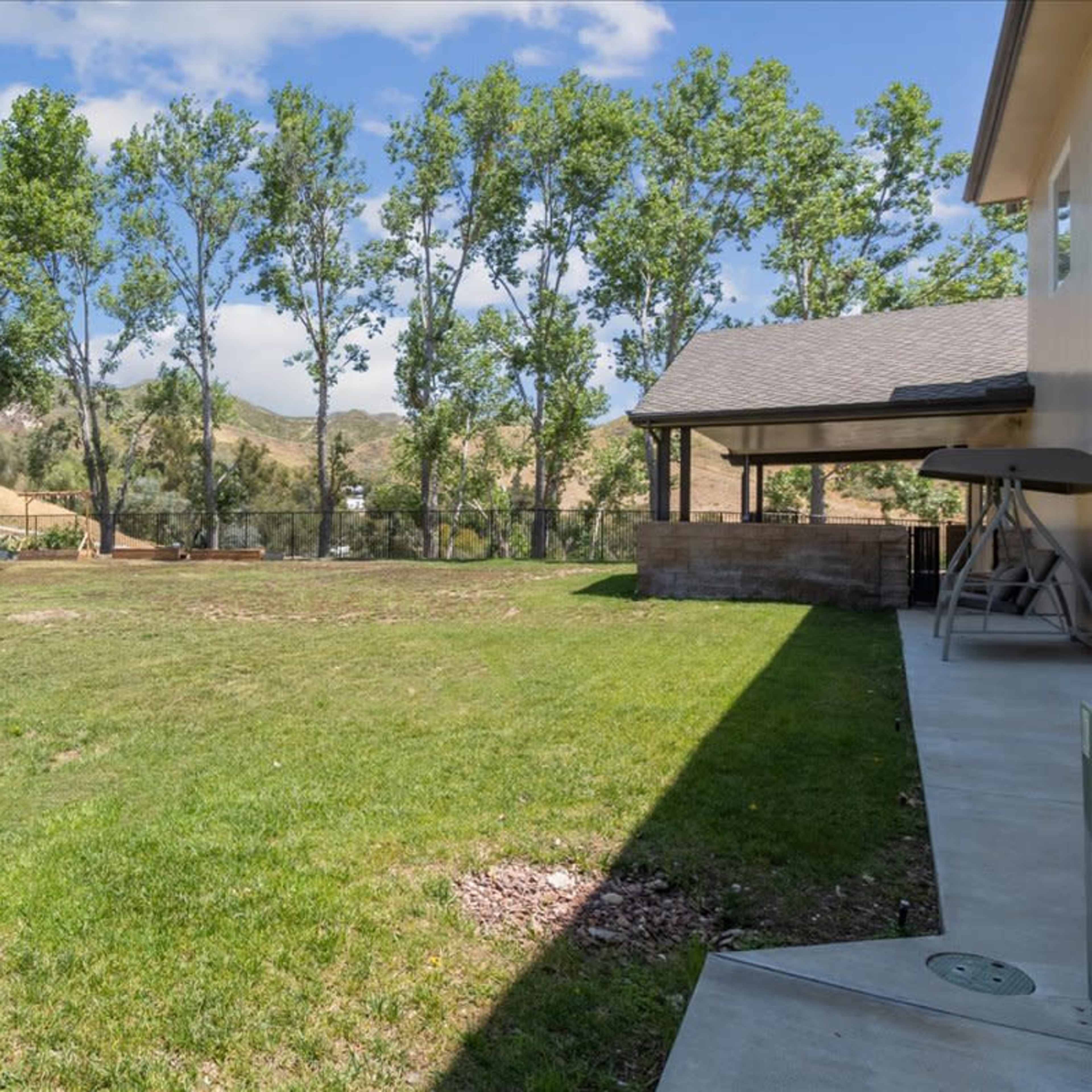 A grassy backyard area bordered by trees, with a view of rolling hills in the background and a patio on the right.