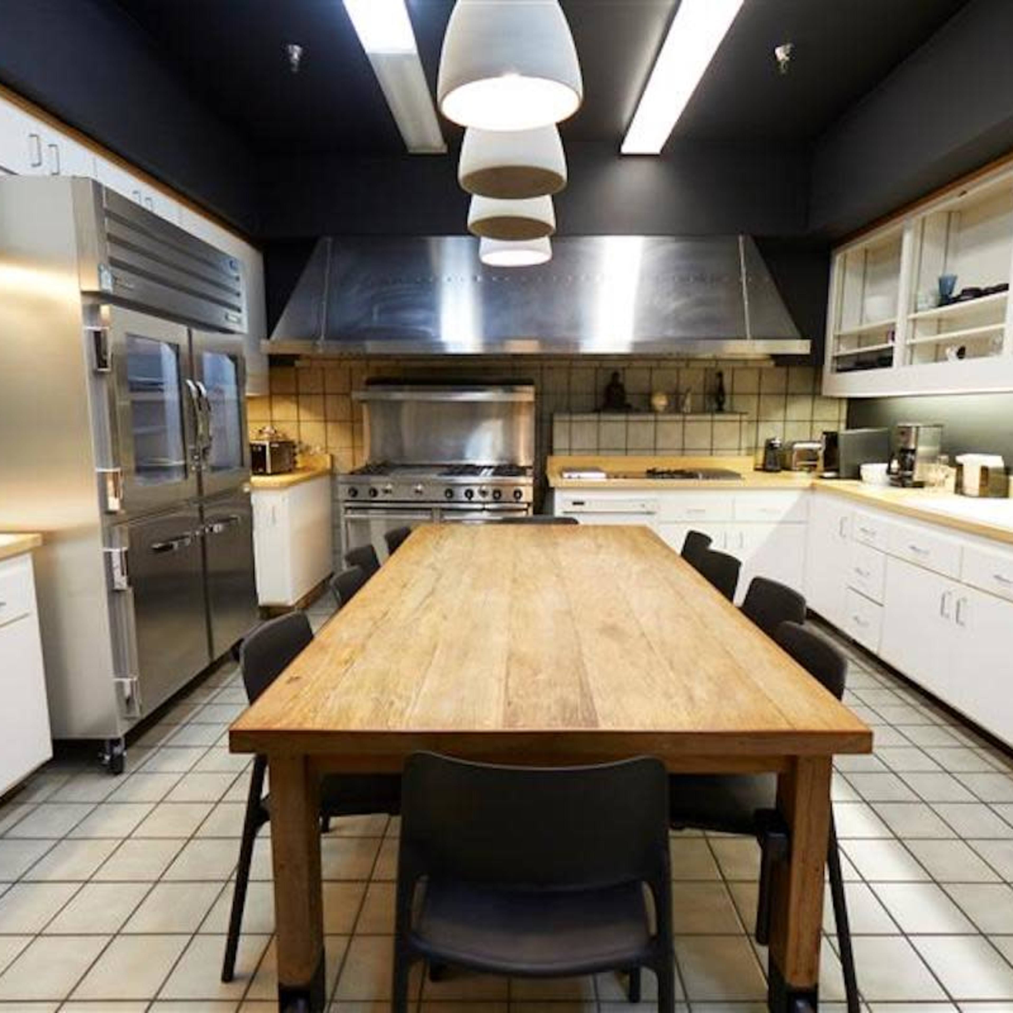 A modern kitchen with stainless steel appliances, a large wooden dining table, and white cabinetry.