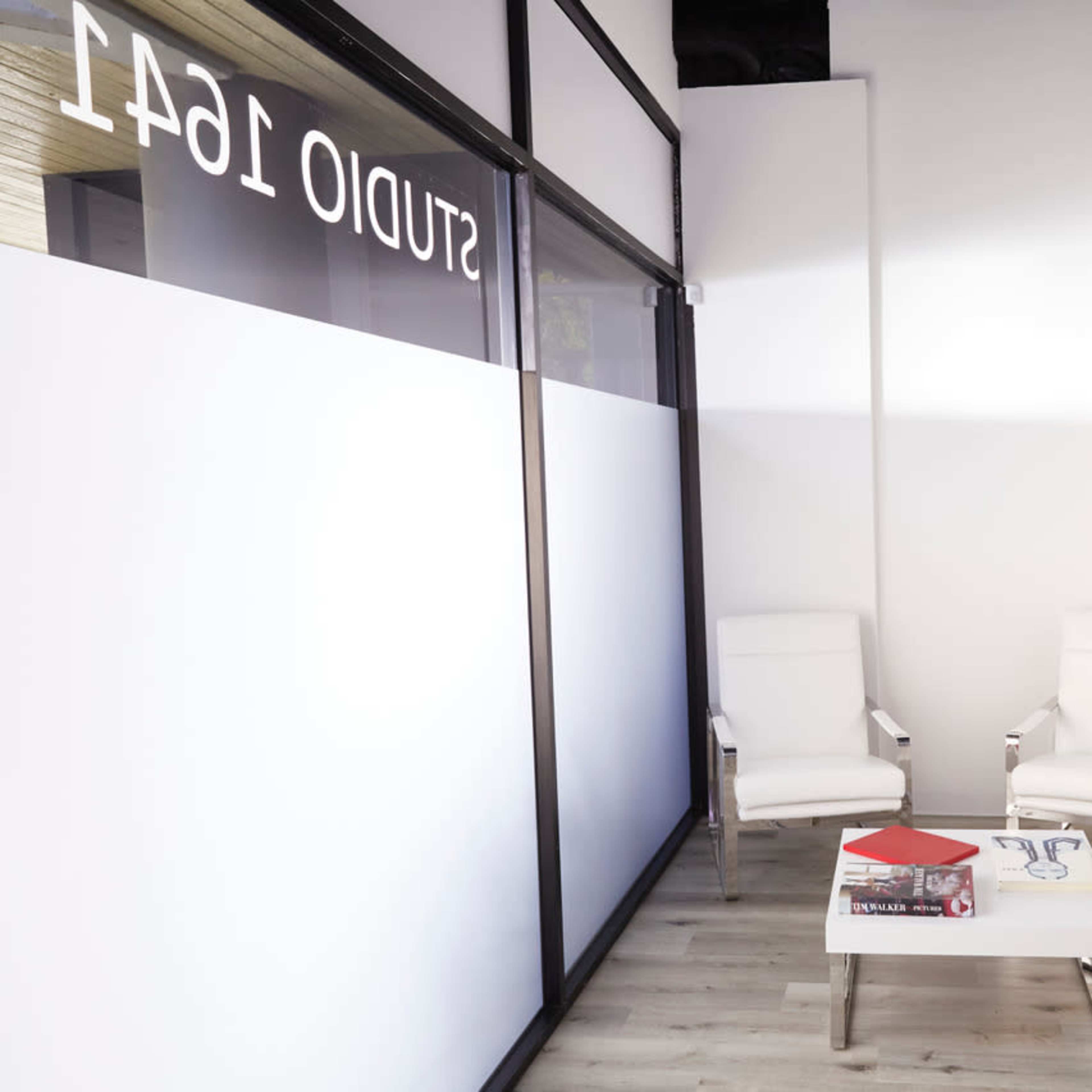 A minimalist waiting area with two white chairs, a small coffee table, and a floor lamp in a well-lit space.