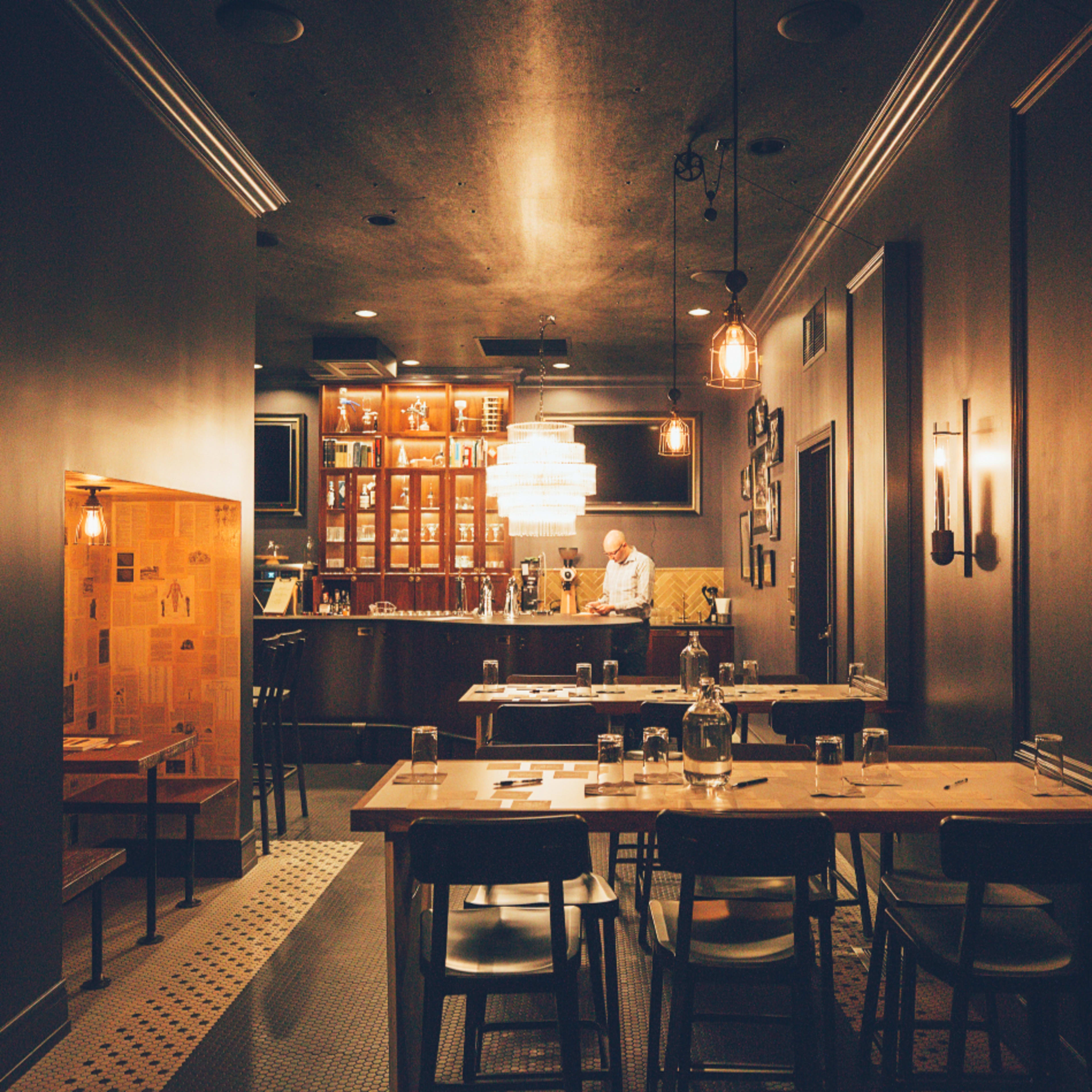 A dimly lit restaurant interior features a bar with wooden shelves and a table setup for dining.