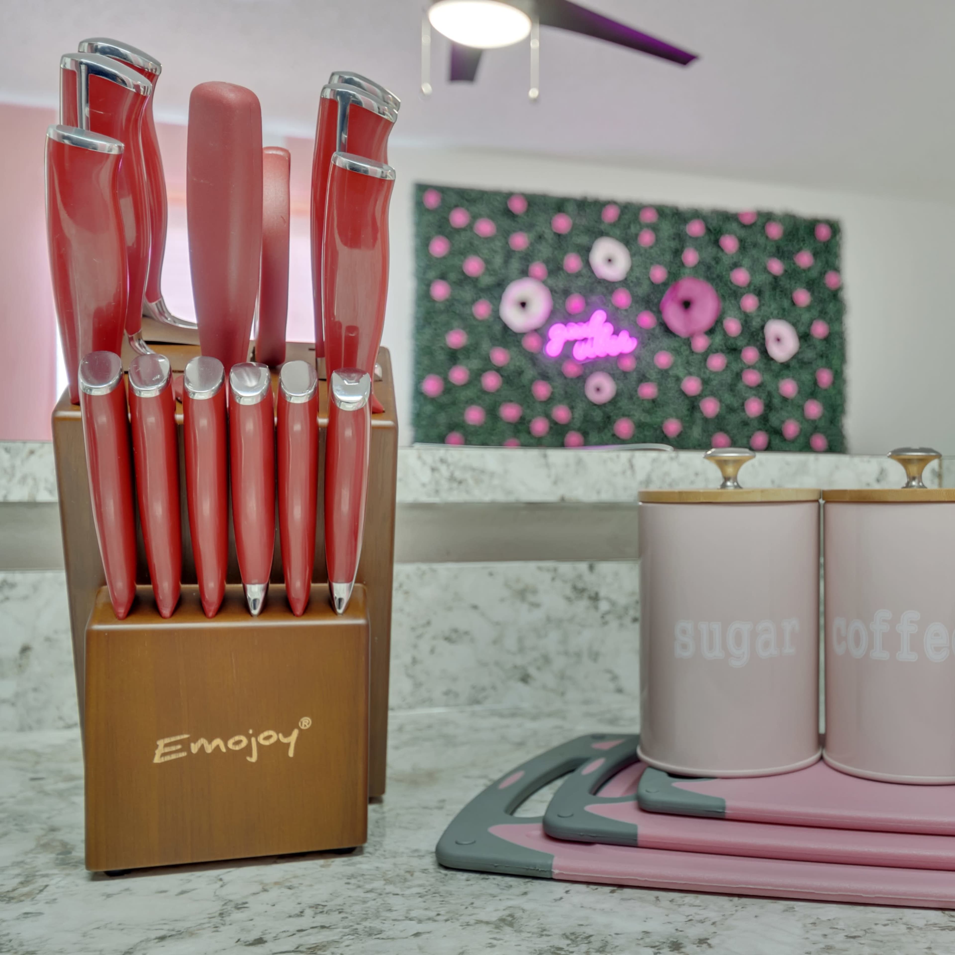 A wooden knife block holds pink knives beside three pink canisters labeled "sugar," "coffee," and "tea" on a counter.