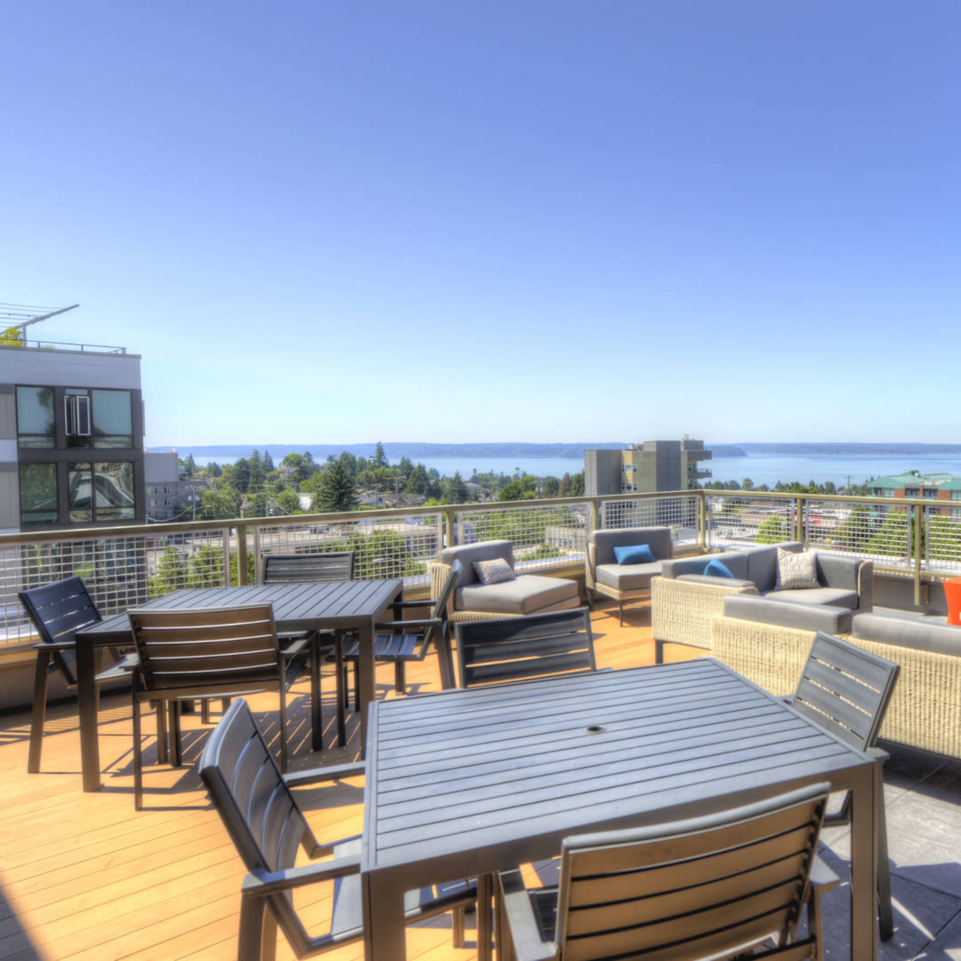 A rooftop terrace with modern seating arrangements, a dining table, and a view of the coastline and distant mountains.