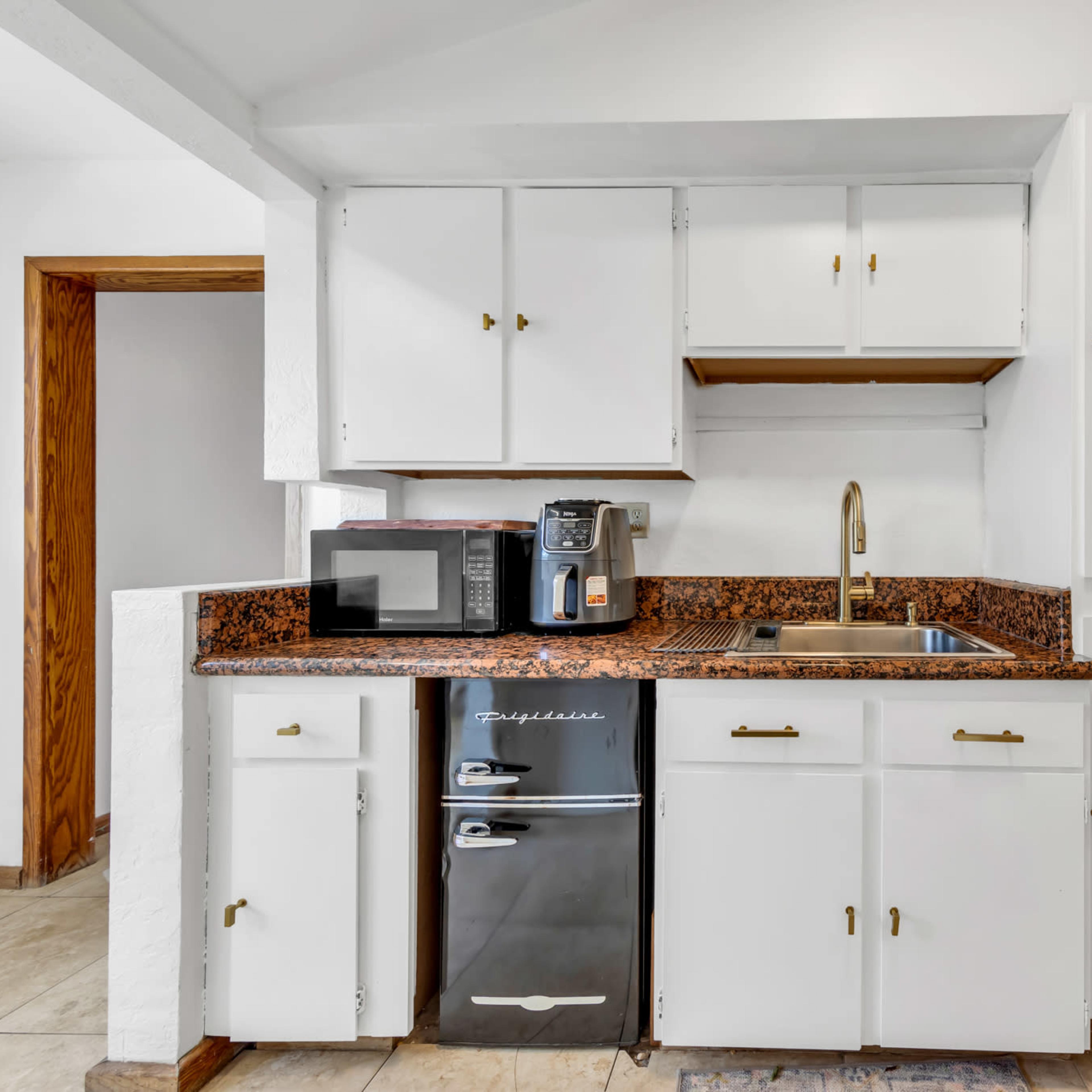 A small kitchen area with white cabinets, a sink, a microwave, and a black refrigerator on a granite countertop.