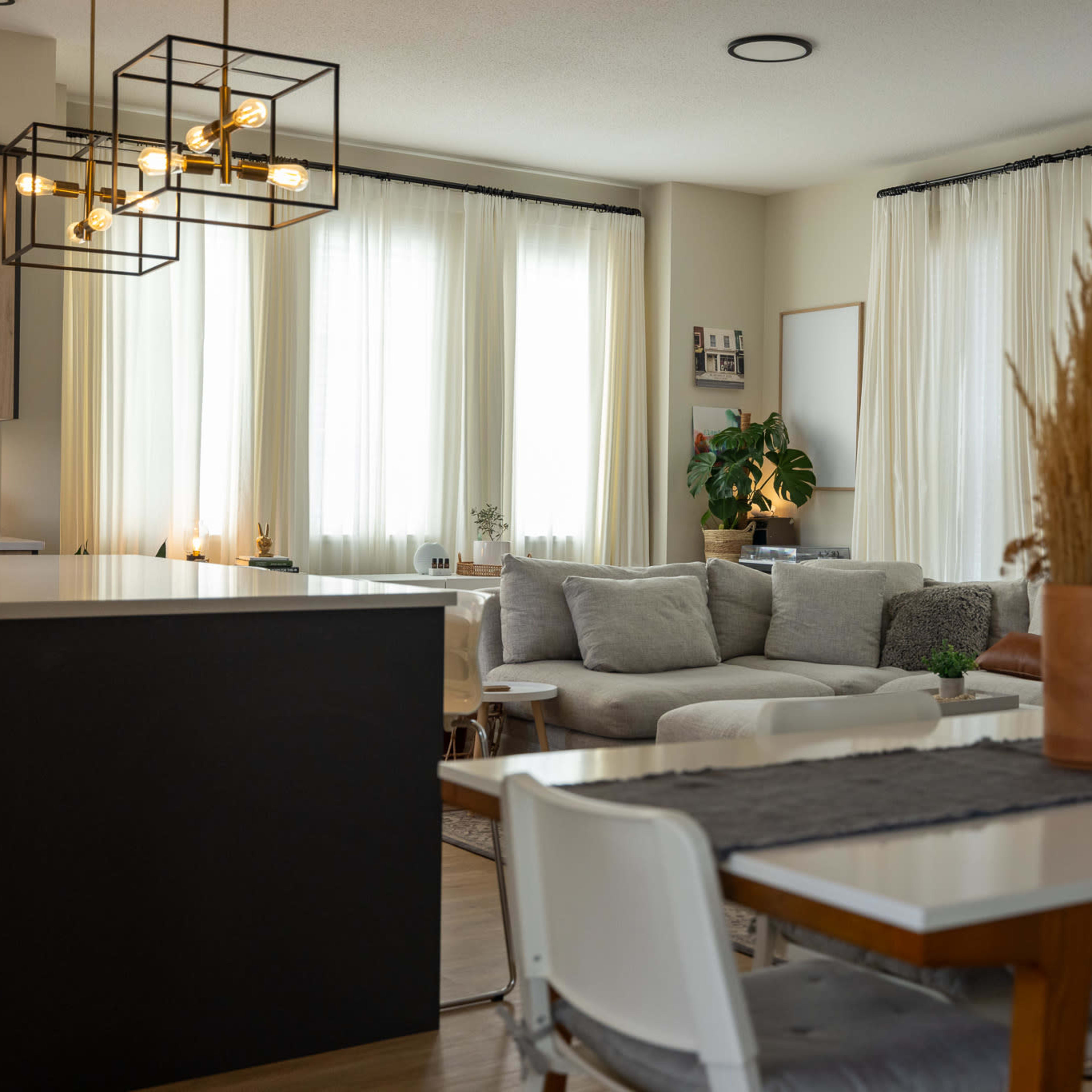 A modern open living space with a kitchen, dining area, and a comfortable seating area featuring large windows and light-colored furnishings.