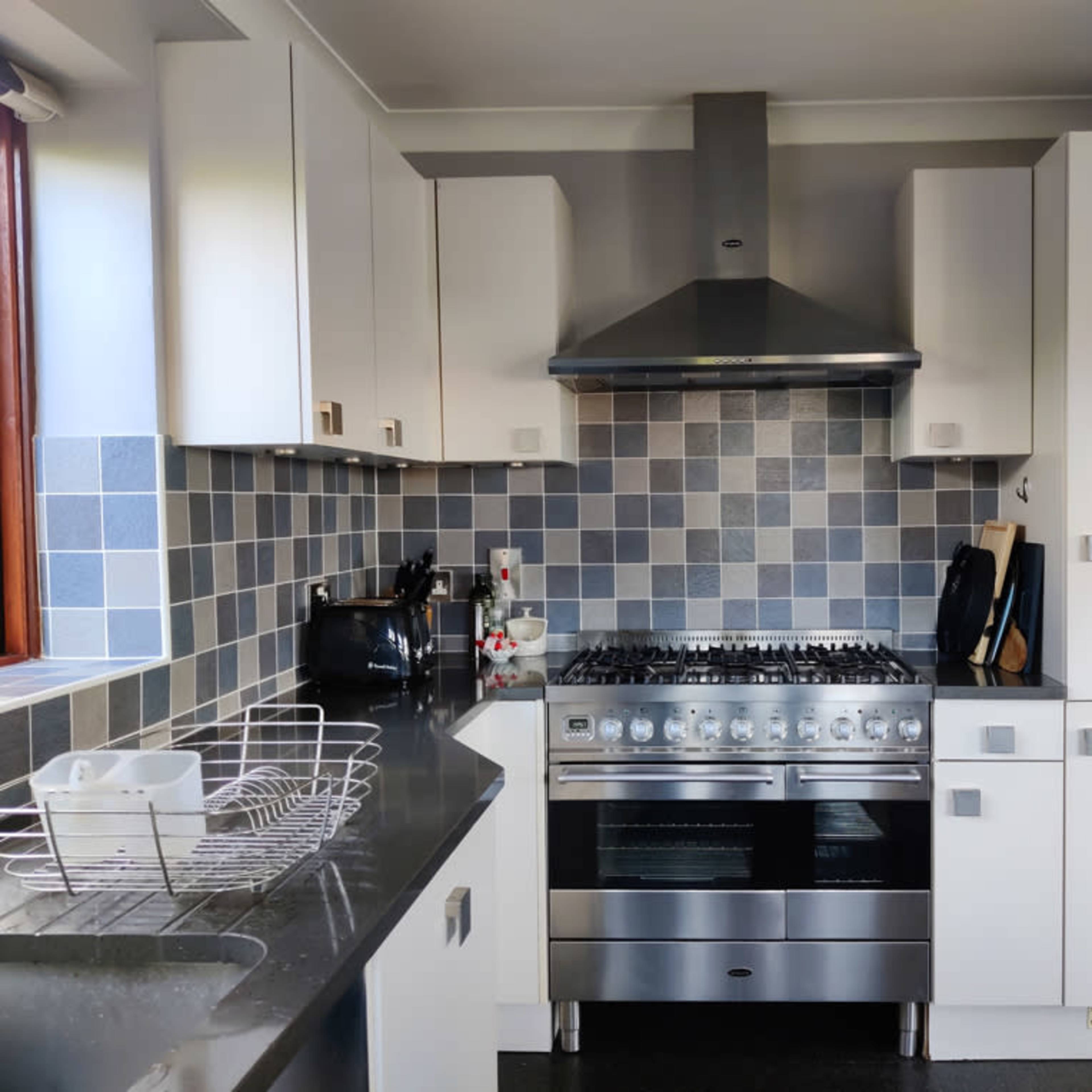 A modern kitchen with a stainless steel gas range, white cabinetry, and a tiled backsplash in shades of gray.