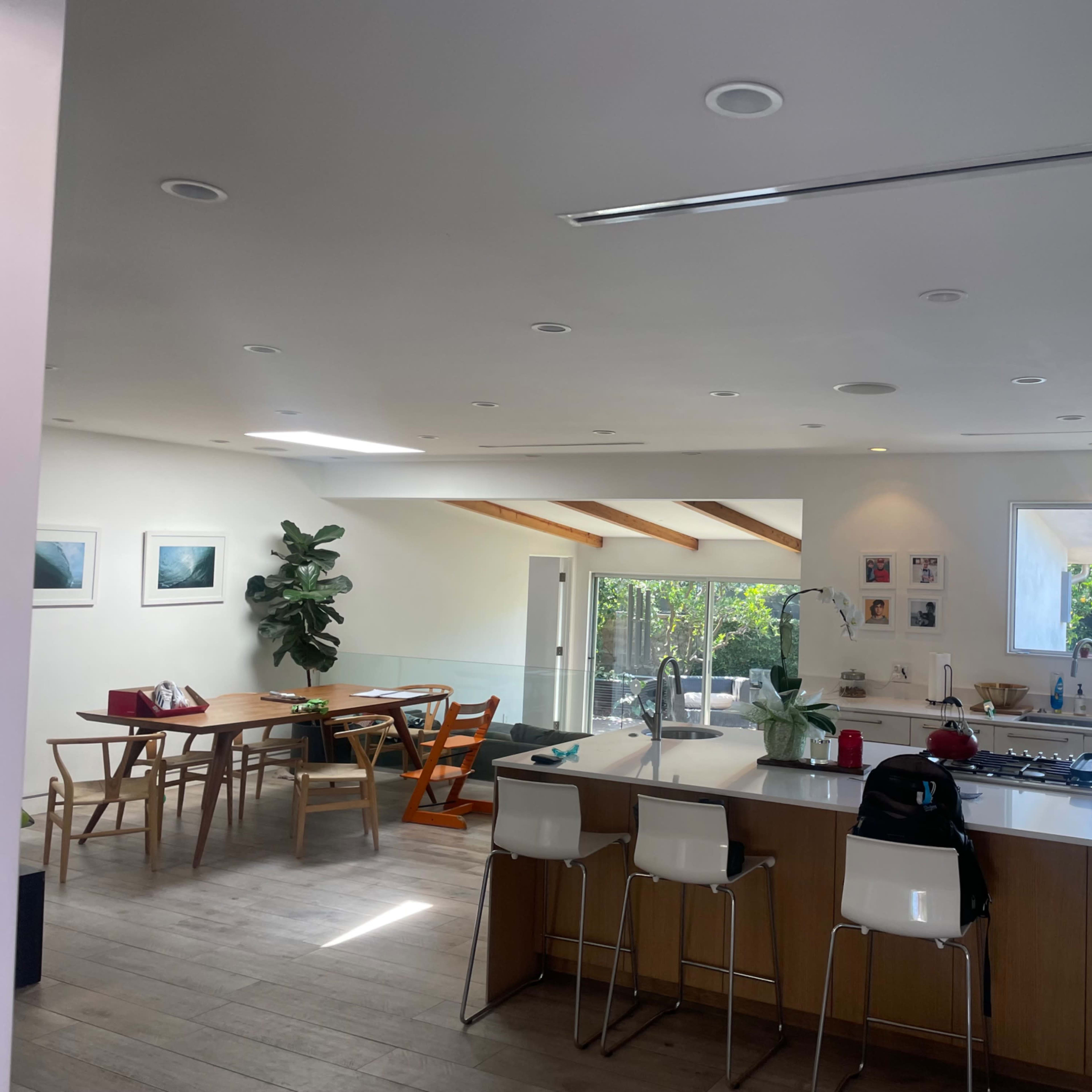 A modern kitchen and dining area featuring a large island, wooden dining table, and large windows with greenery visible outside.