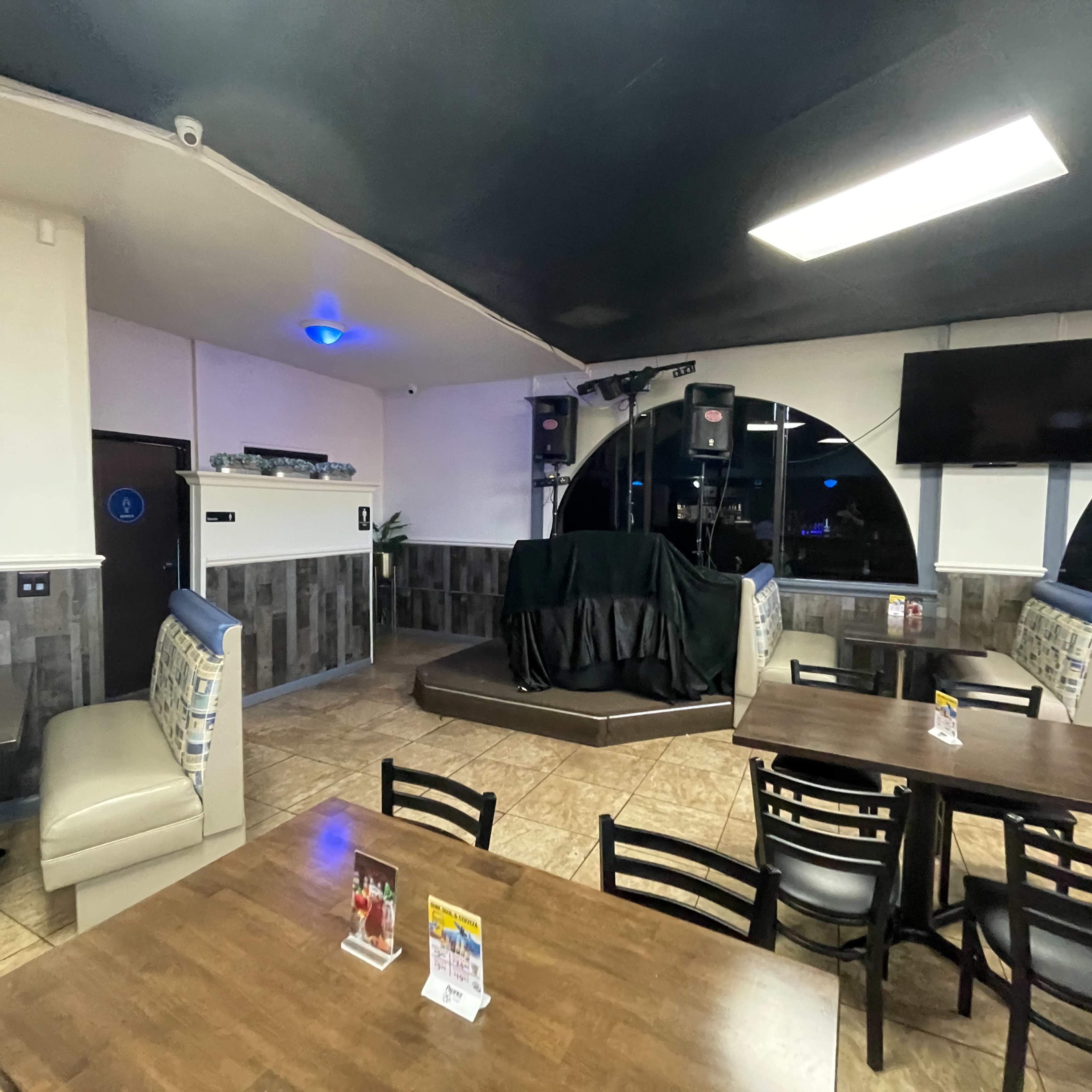An empty restaurant interior with tables, chairs, and a stage area covered by a black cloth.