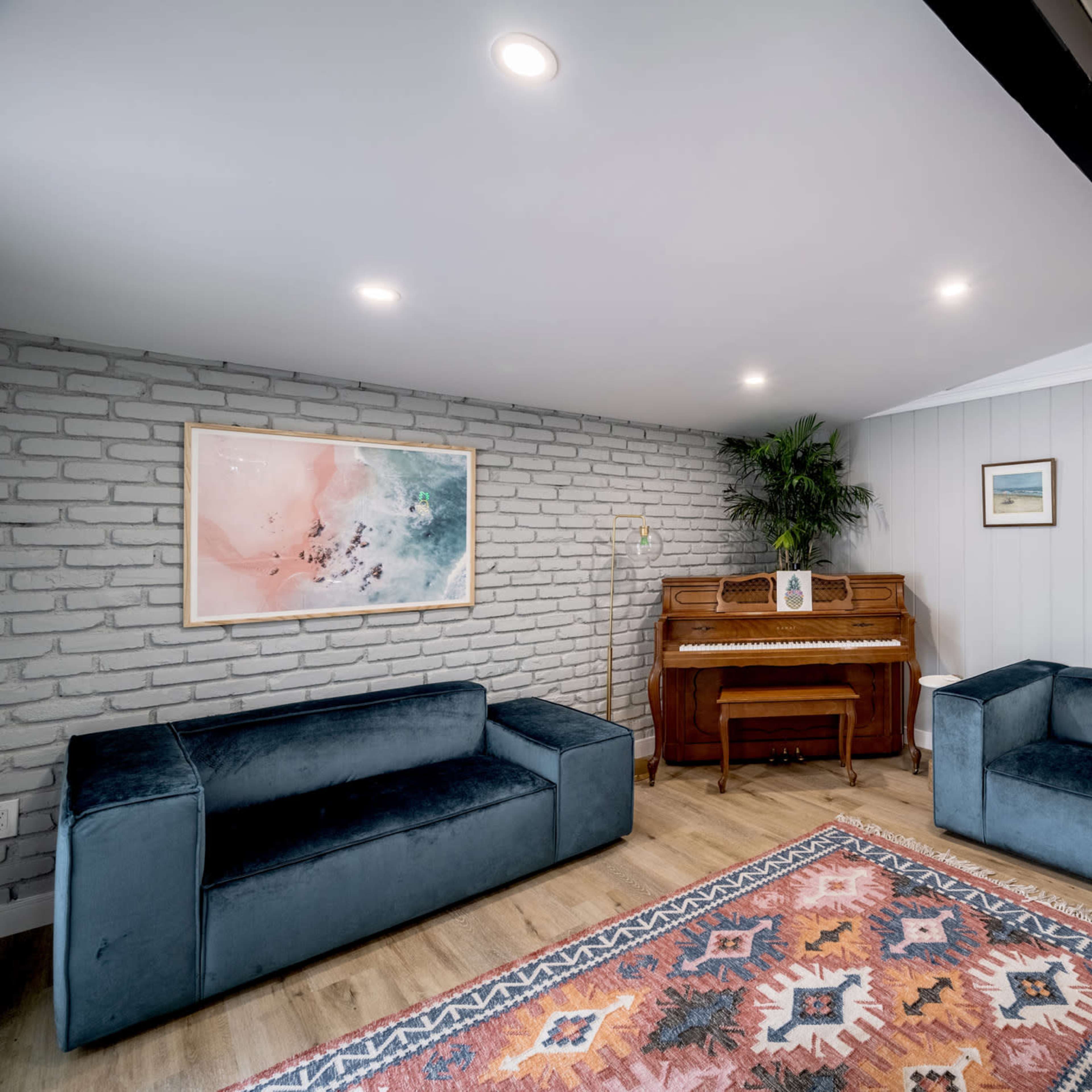 A modern interior space featuring two blue couches, a wooden piano, and a decorative rug on the floor, against a backdrop of gray brick and light-colored walls.