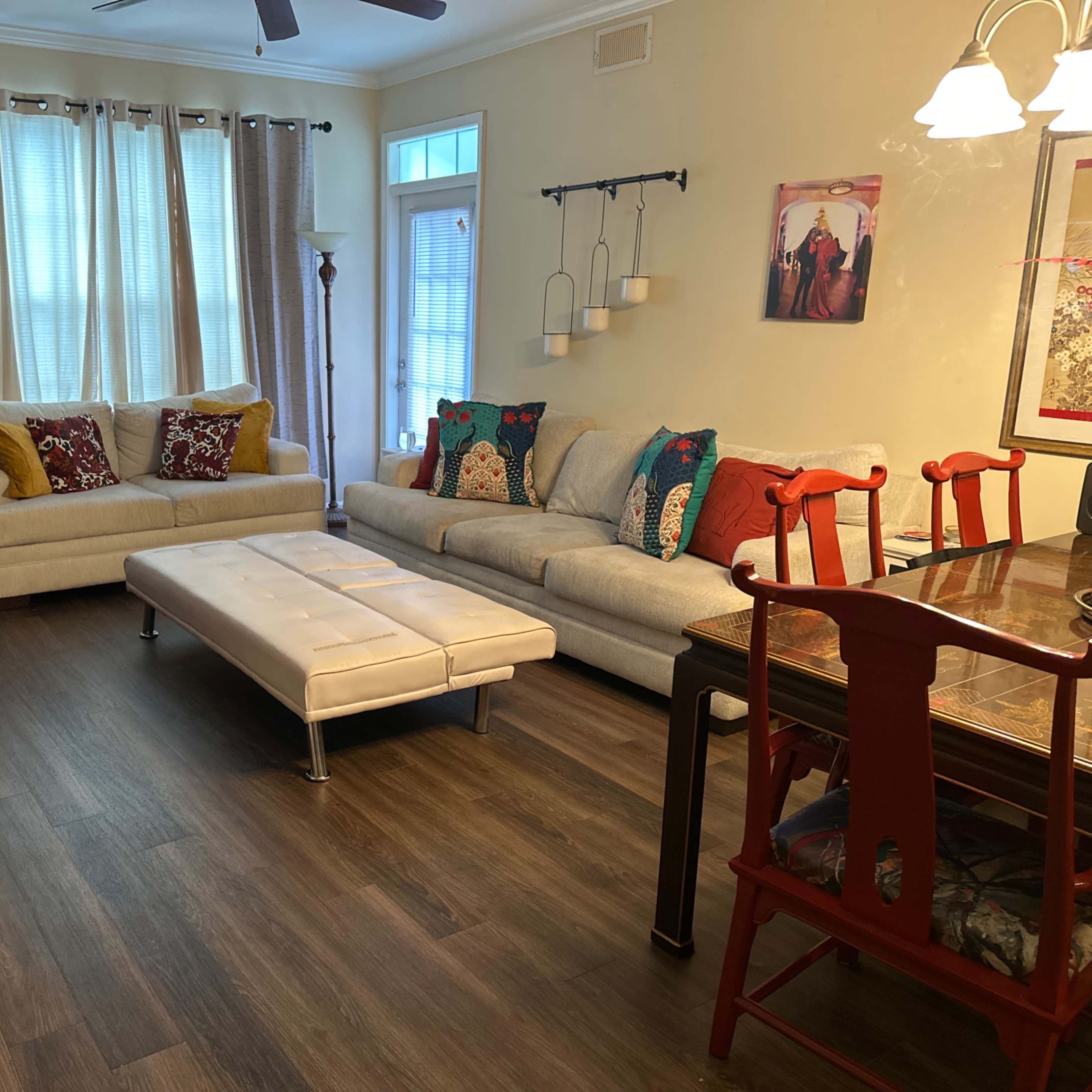 A cozy living room with two light-colored sofas, a coffee table in the center, and a dining area featuring a wooden table and red chairs.