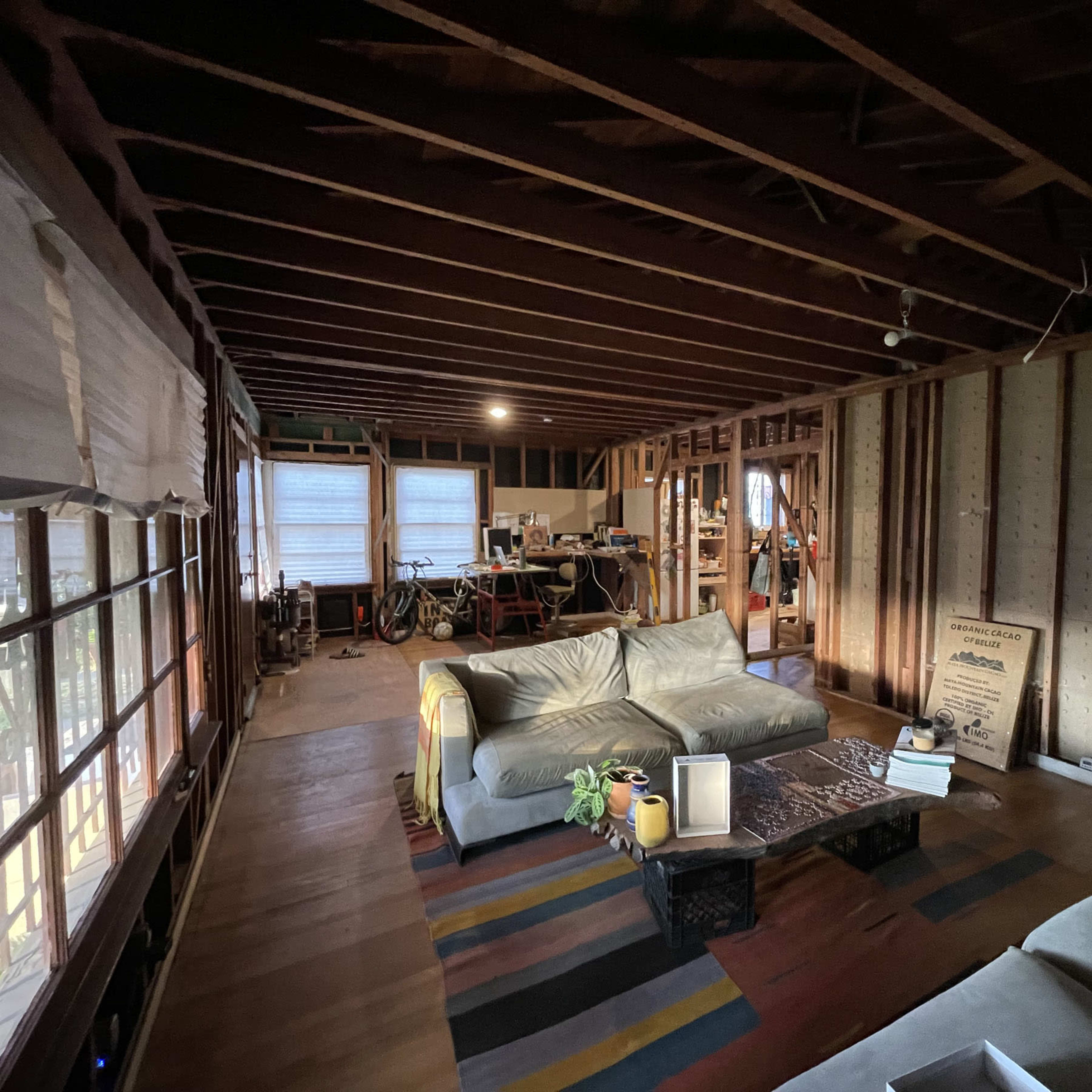 An interior space with exposed beams, featuring two sofas, a coffee table, and a workspace in the background.