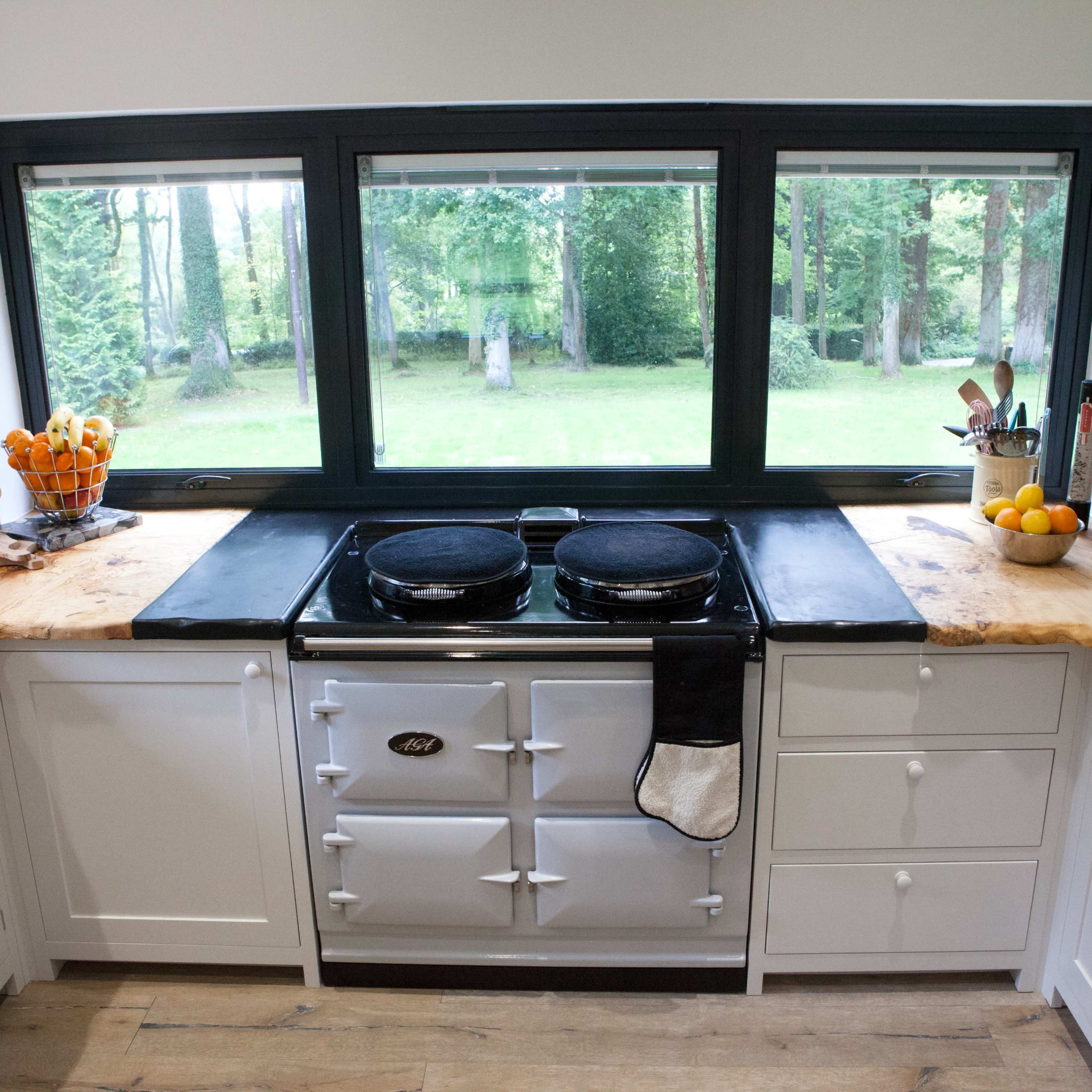 A modern kitchen with a wood countertop and a traditional stove beneath a large window overlooking a green outdoor space.