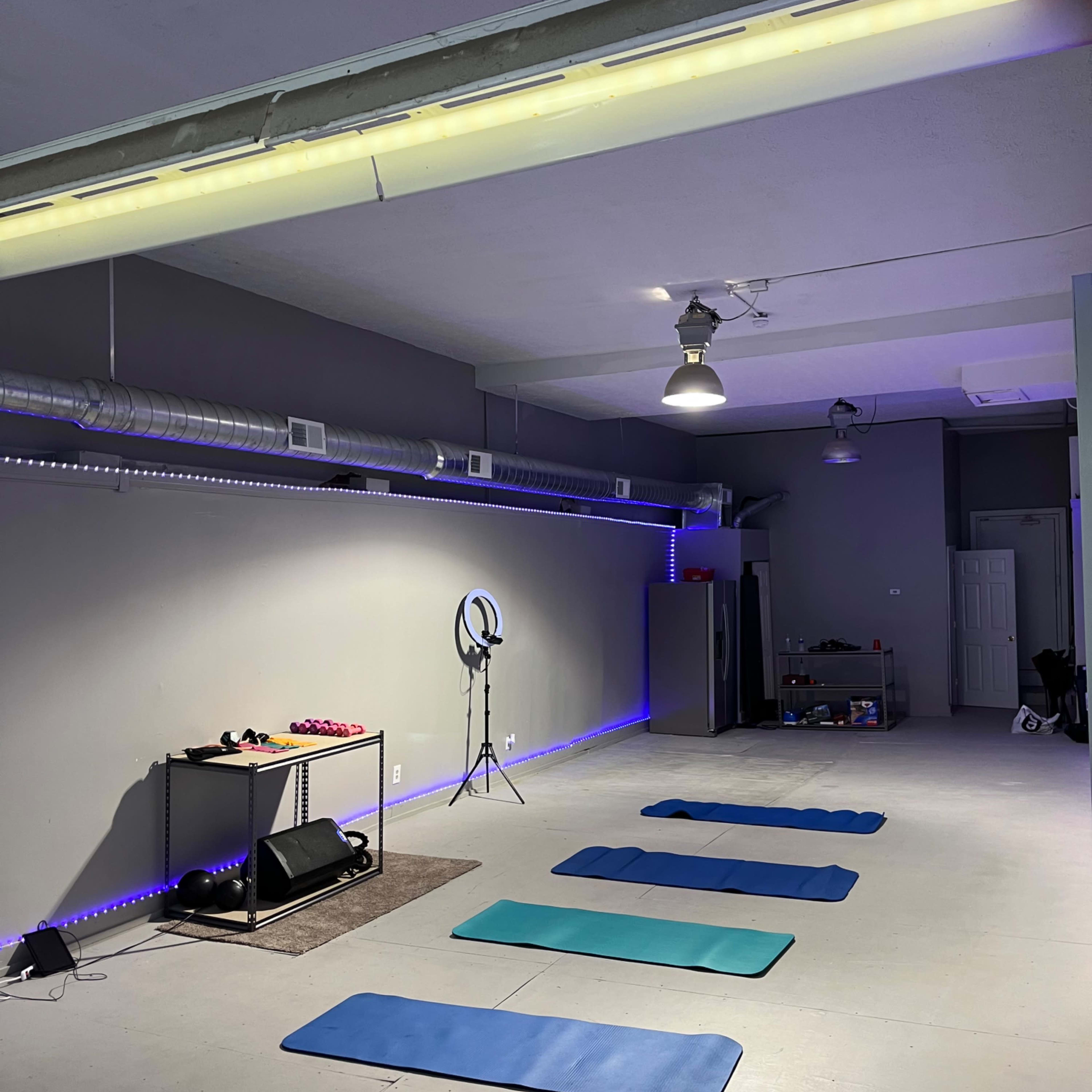 A spacious yoga or exercise studio with several mats arranged on the floor, a mirror, and lights along the walls.
