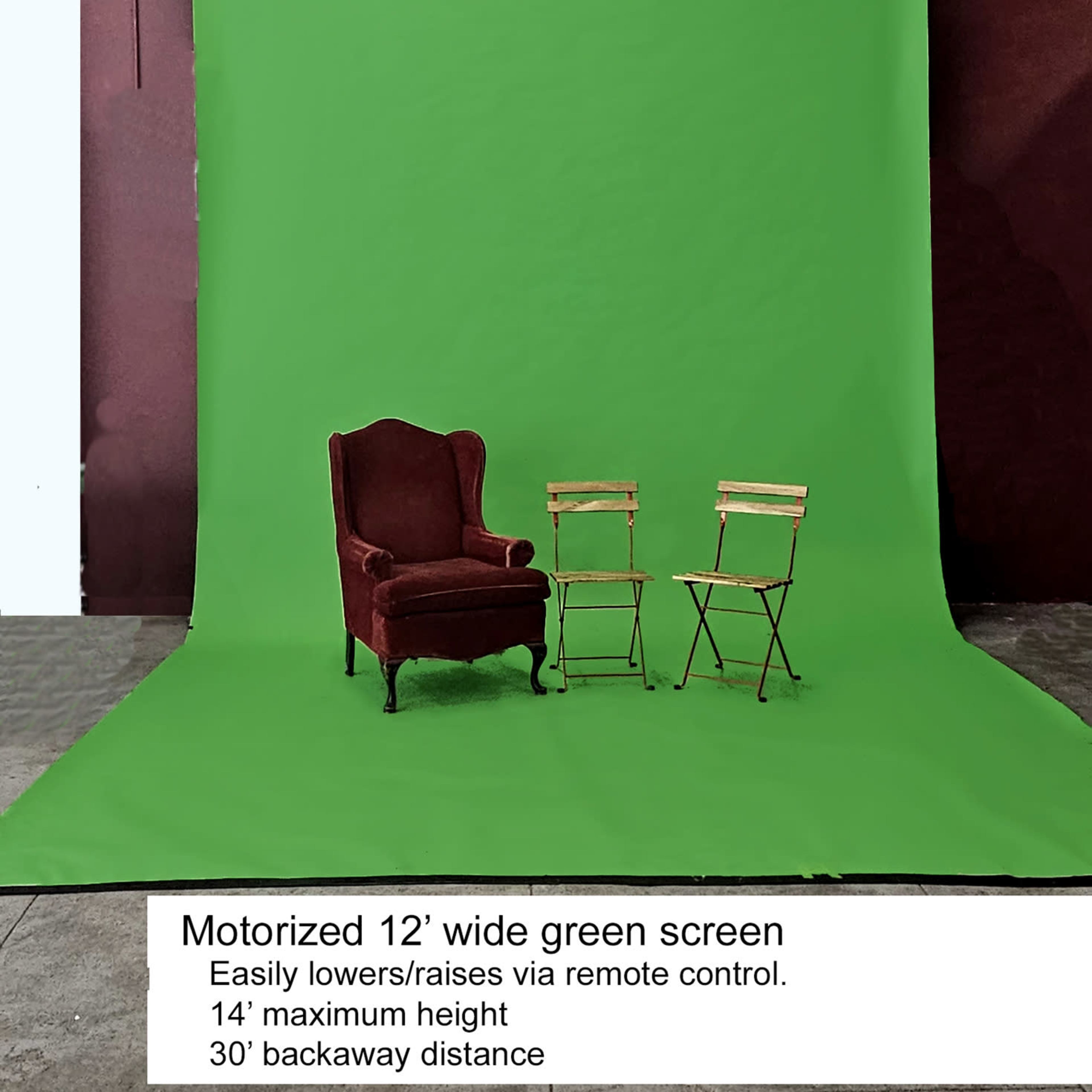 A motorized 12-foot wide green screen set up in an indoor space, accompanied by a red upholstered armchair and two wooden director's chairs.