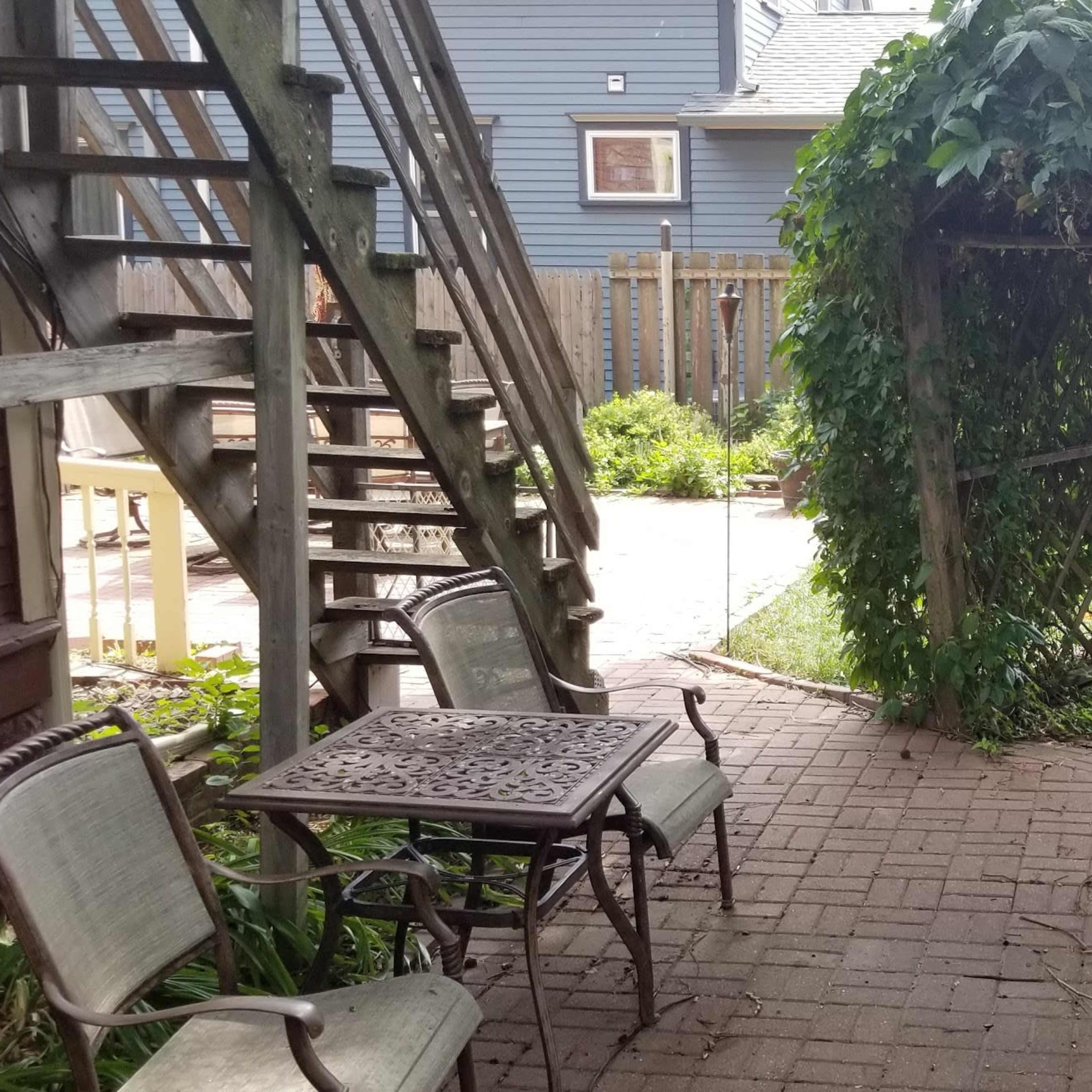A paved walkway leads through a green archway of vines toward a backyard with seating and a statue.