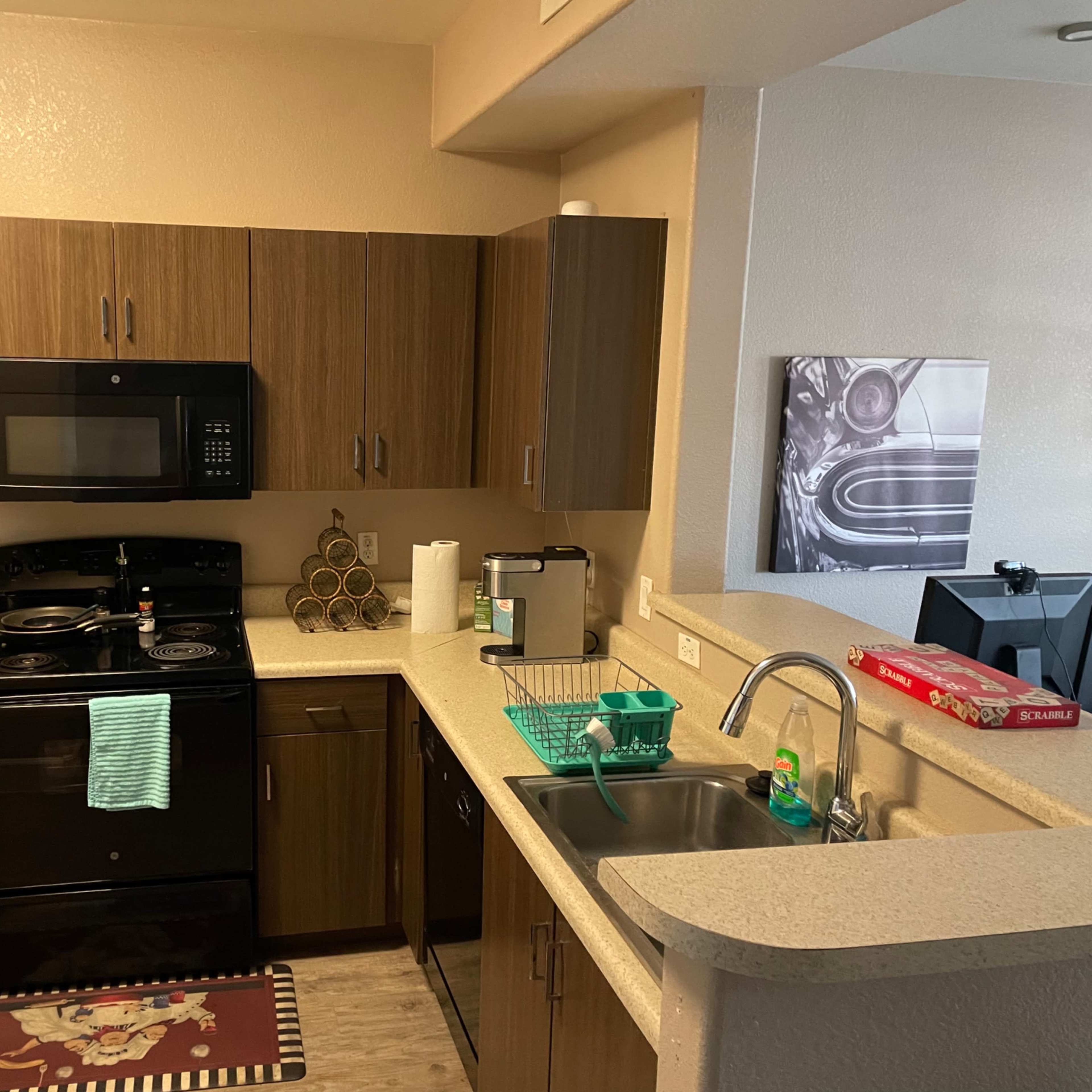 A compact kitchen with dark wood cabinetry, a black stove and microwave, and a countertop with a sink and various kitchen items.