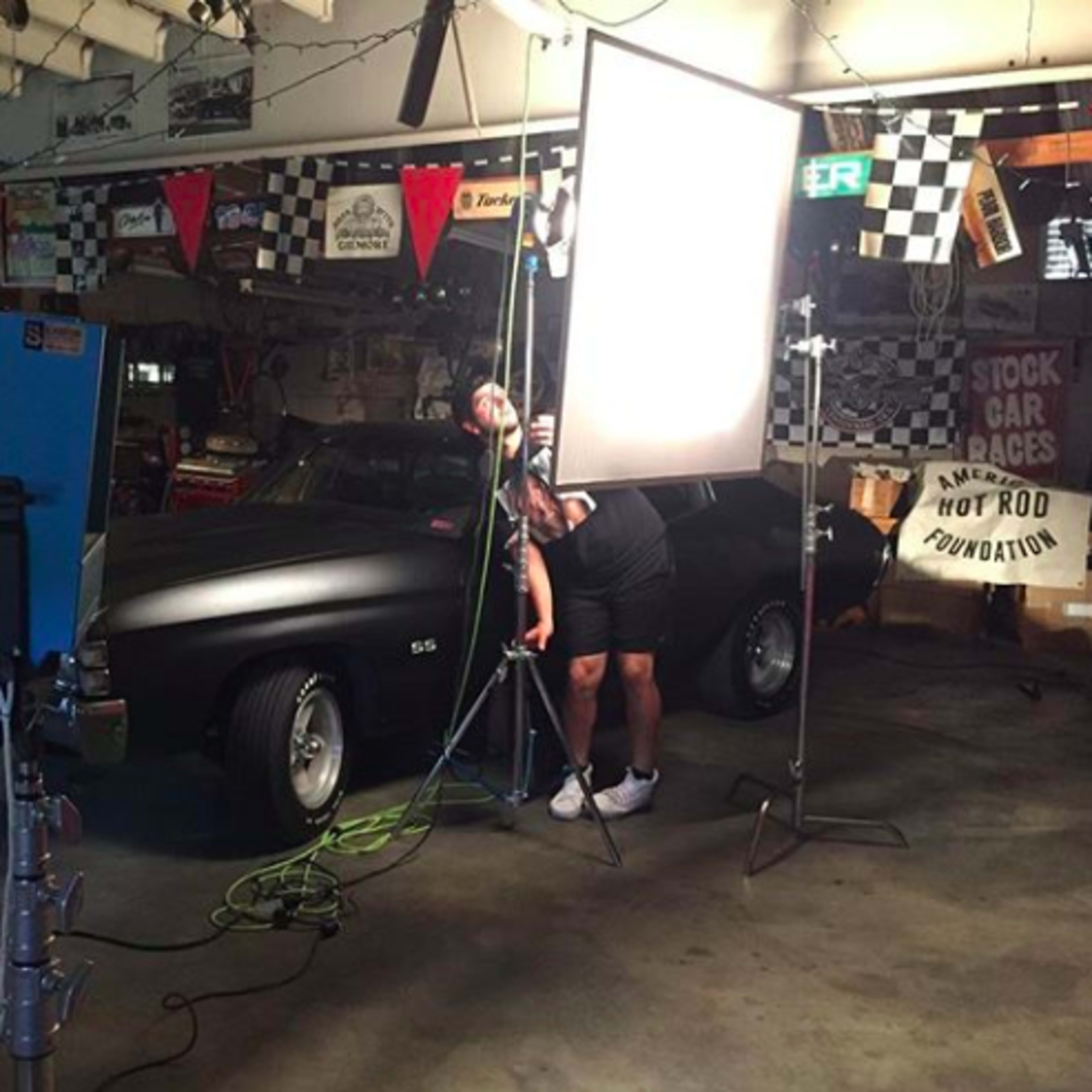 A black car is featured in a garage, surrounded by photography equipment and checkered flags.