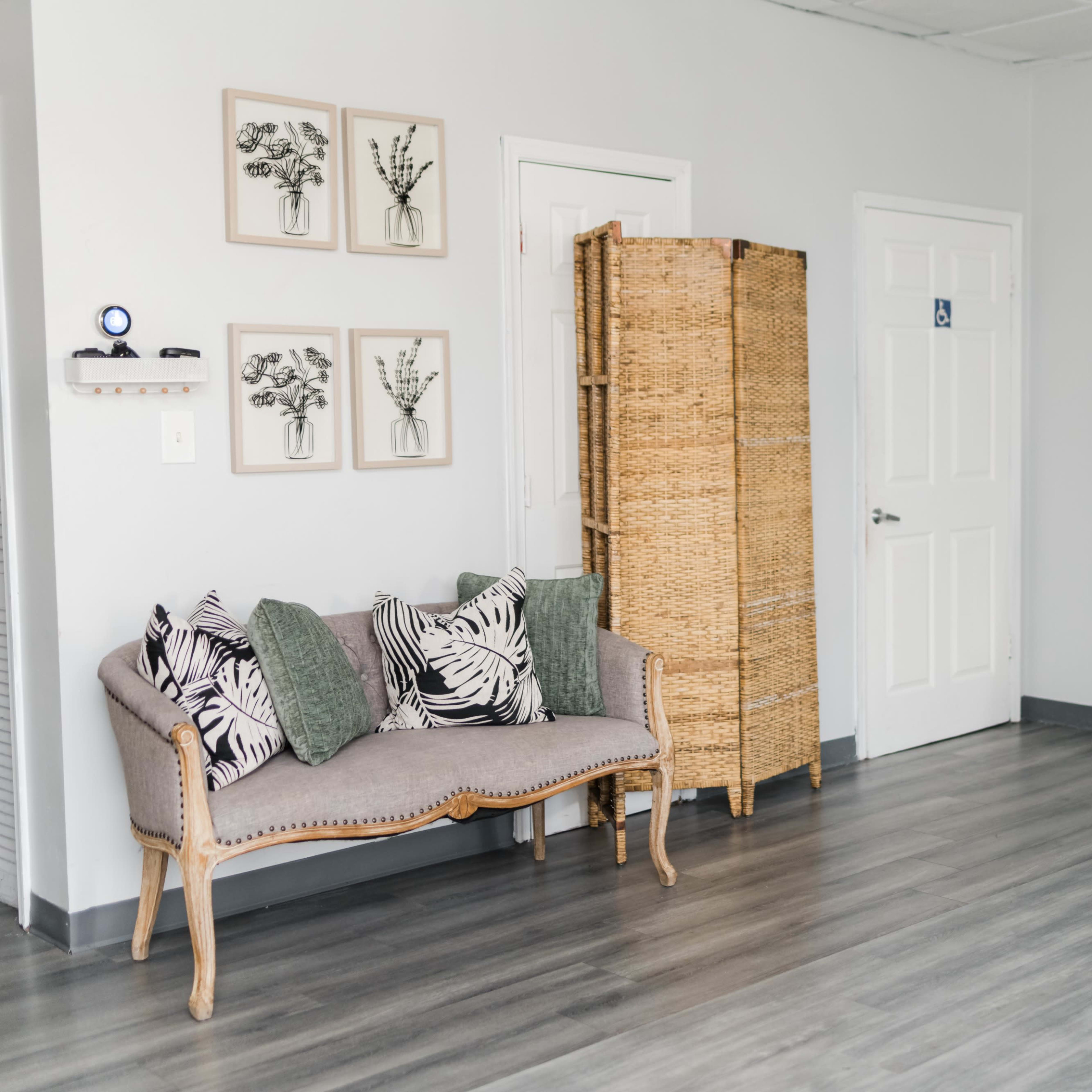 A minimalist interior with a couch, decorative framed artworks on the wall, a wicker screen, and a full-length mirror.