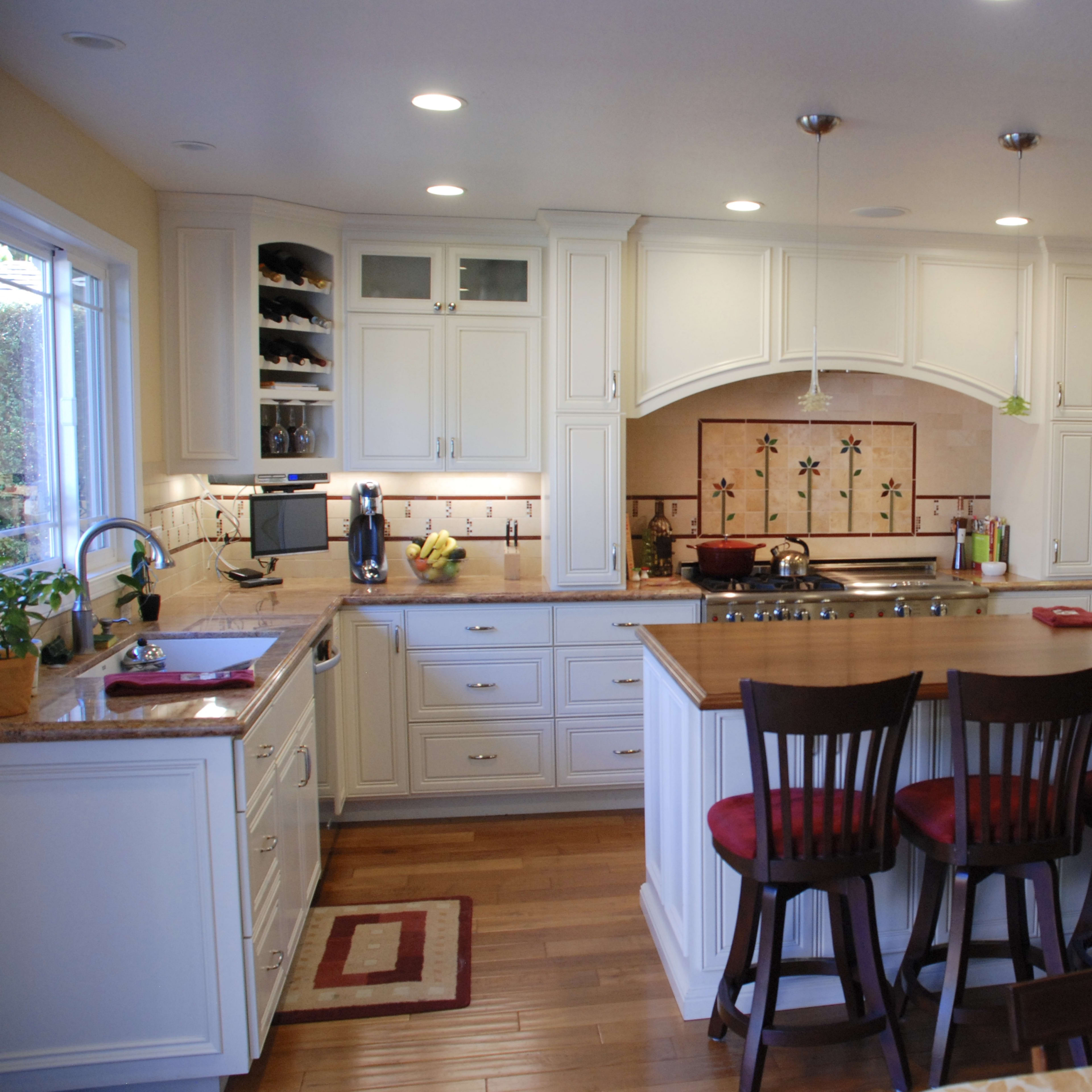 A modern kitchen features white cabinetry, a central island with bar stools, and stainless steel appliances.
