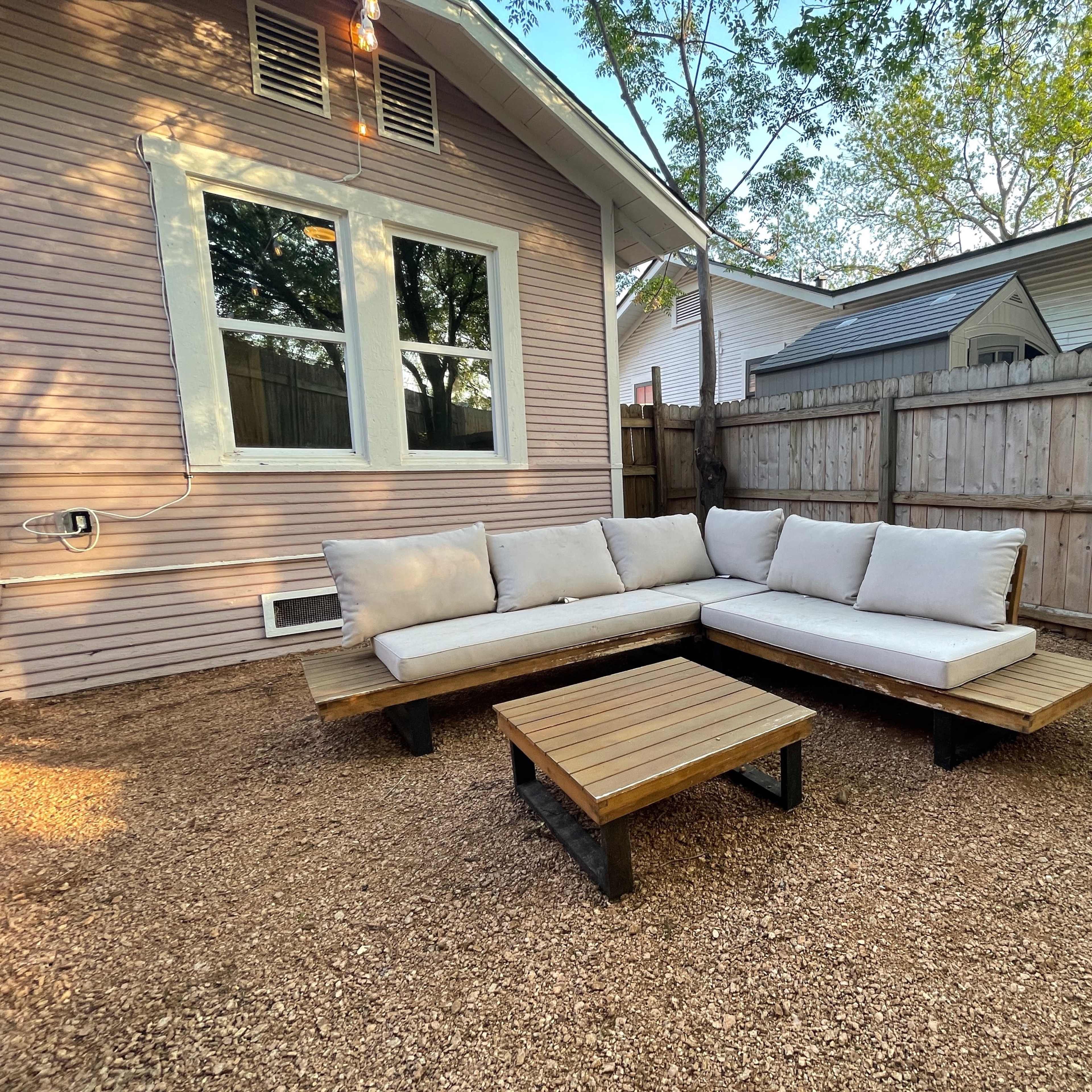 A sectional outdoor seating arrangement with a matching coffee table on a gravel surface in a fenced backyard.