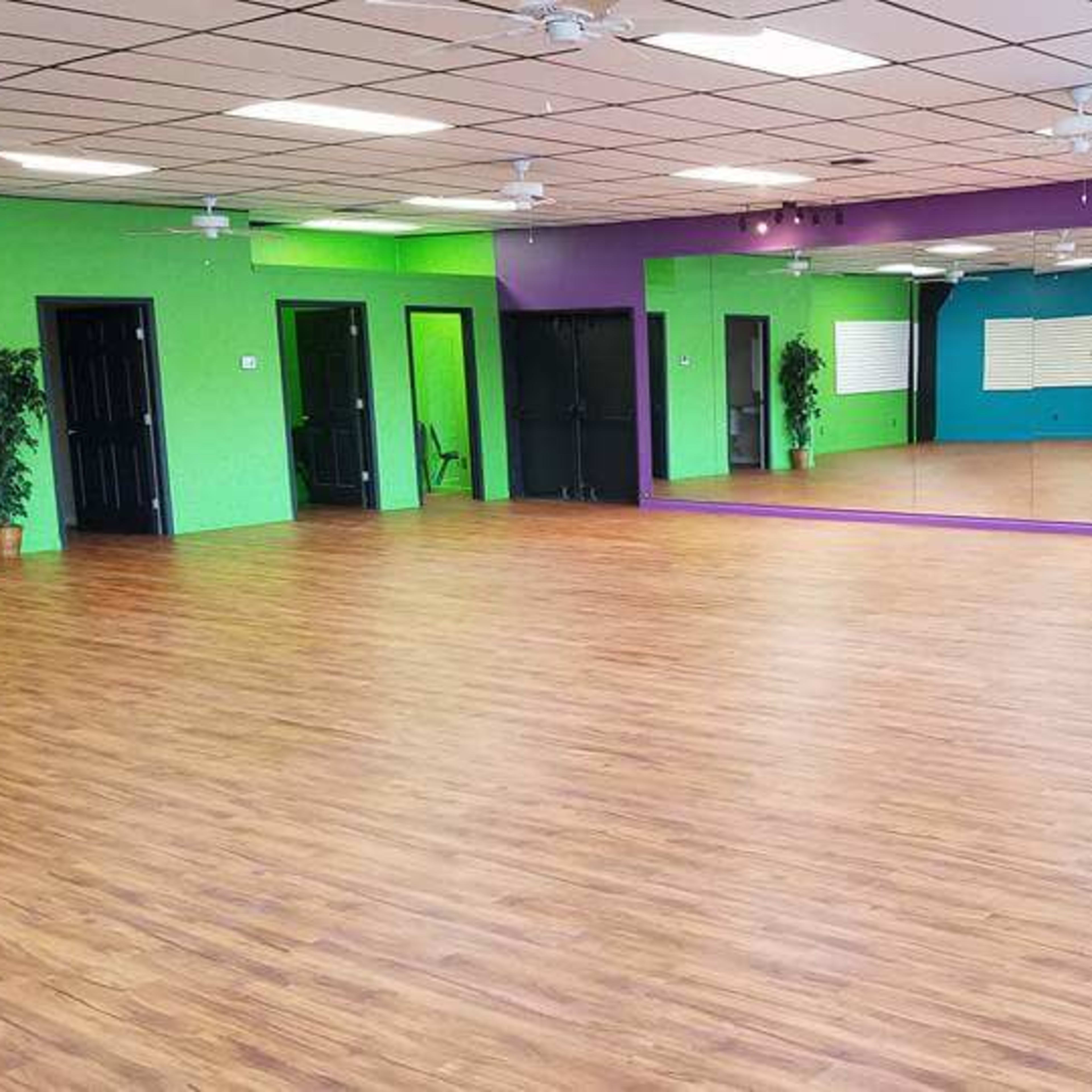 A spacious dance studio featuring wooden floors, mirrors on one wall, and brightly colored painted walls.