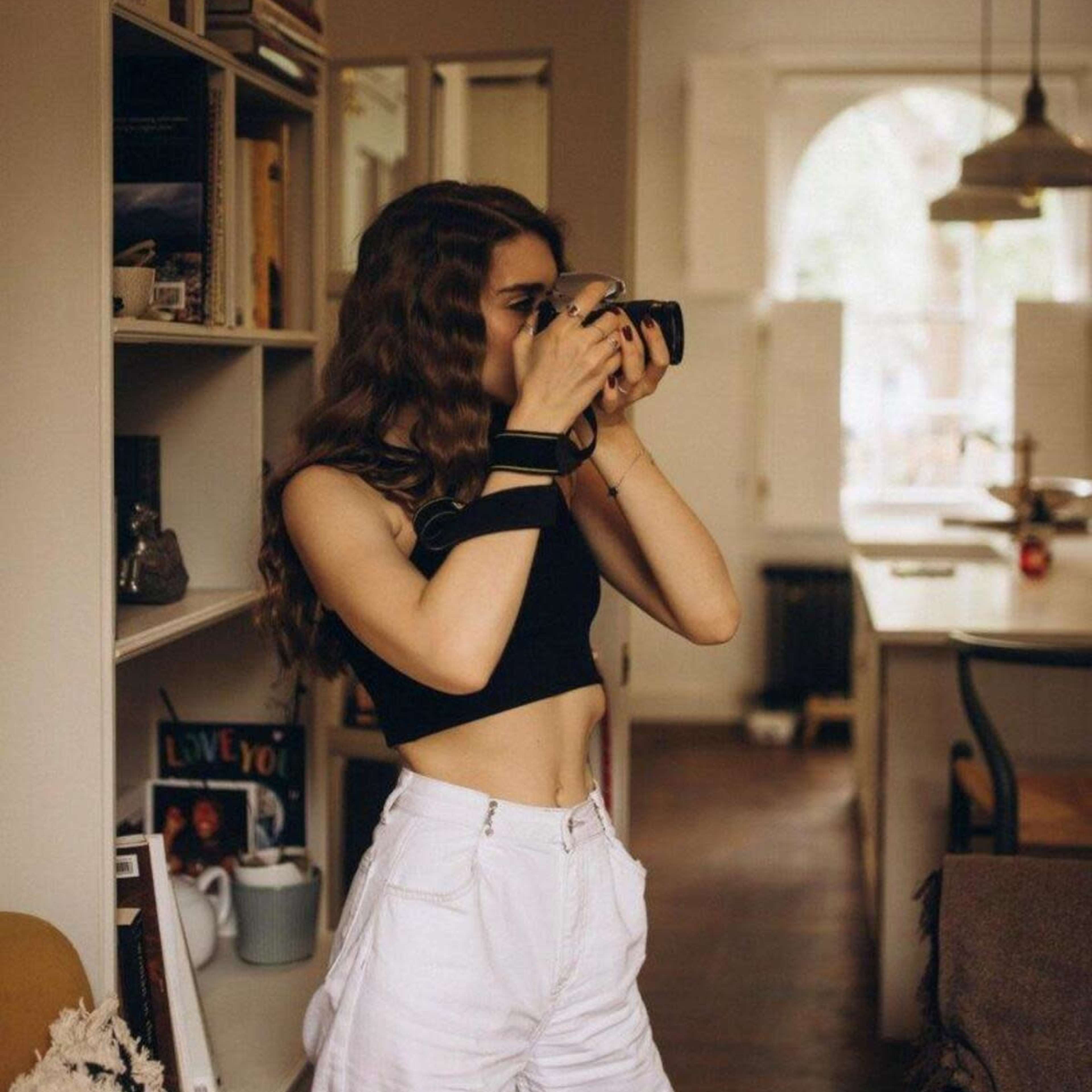 A woman with long hair is taking a photo with a camera in a cozy, well-lit interior space.