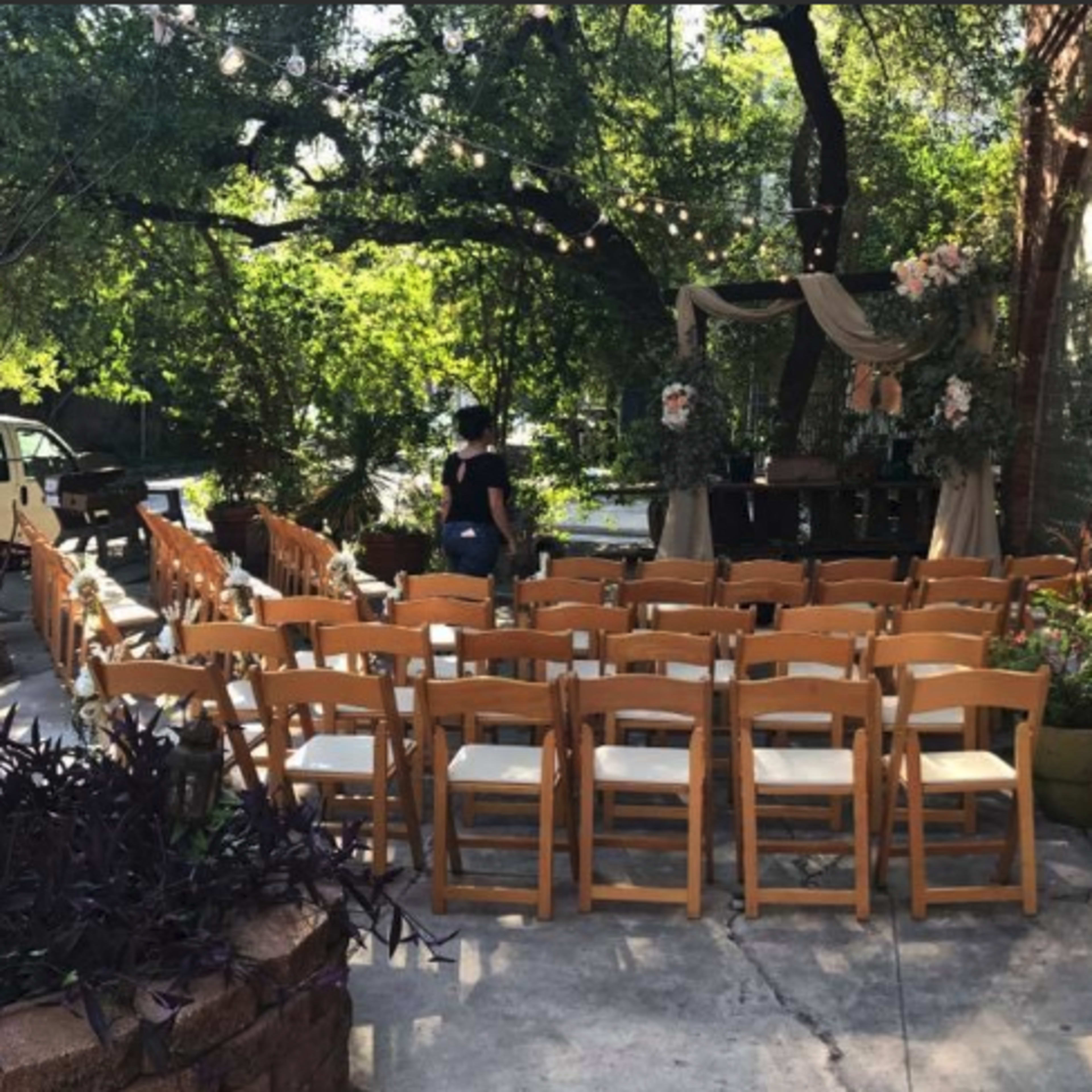 A set of wooden chairs arranged in rows in an outdoor setting decorated with floral arrangements and draped fabric.
