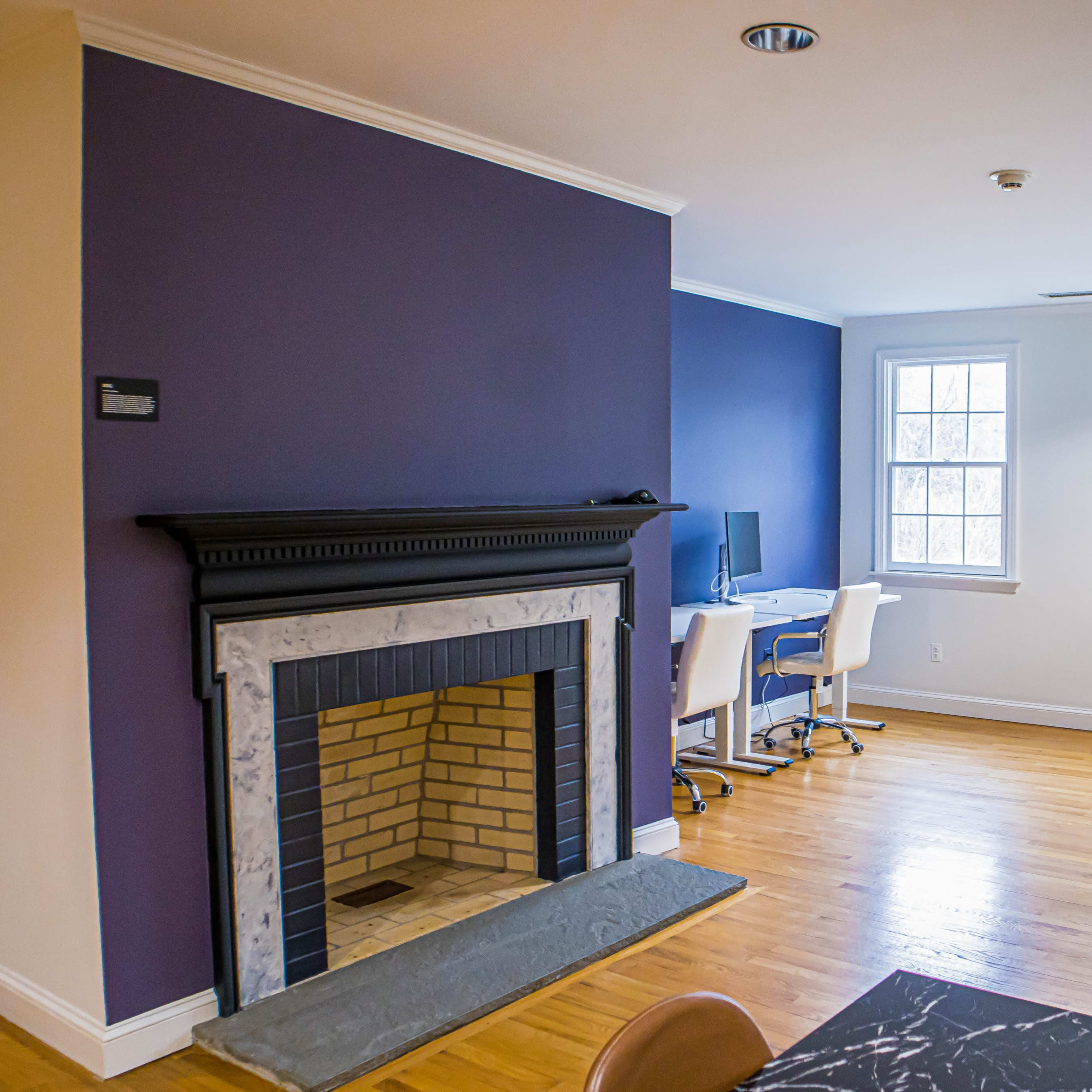 A modern office space featuring a purple wall with a fireplace and several workstations equipped with computers on the opposite side.