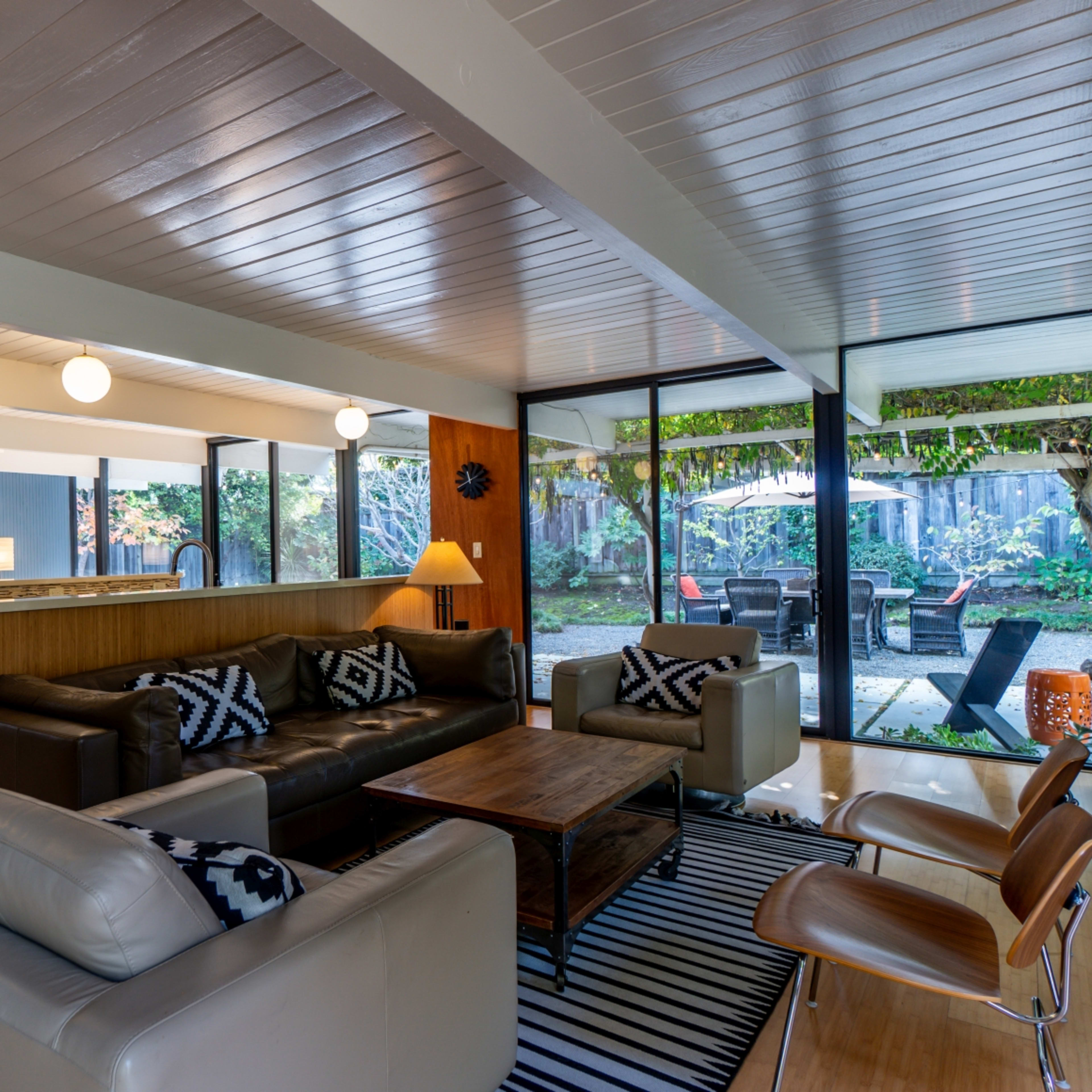 A modern living room featuring a dark sofa and a light-colored armchair, with large glass windows overlooking a landscaped outdoor area.