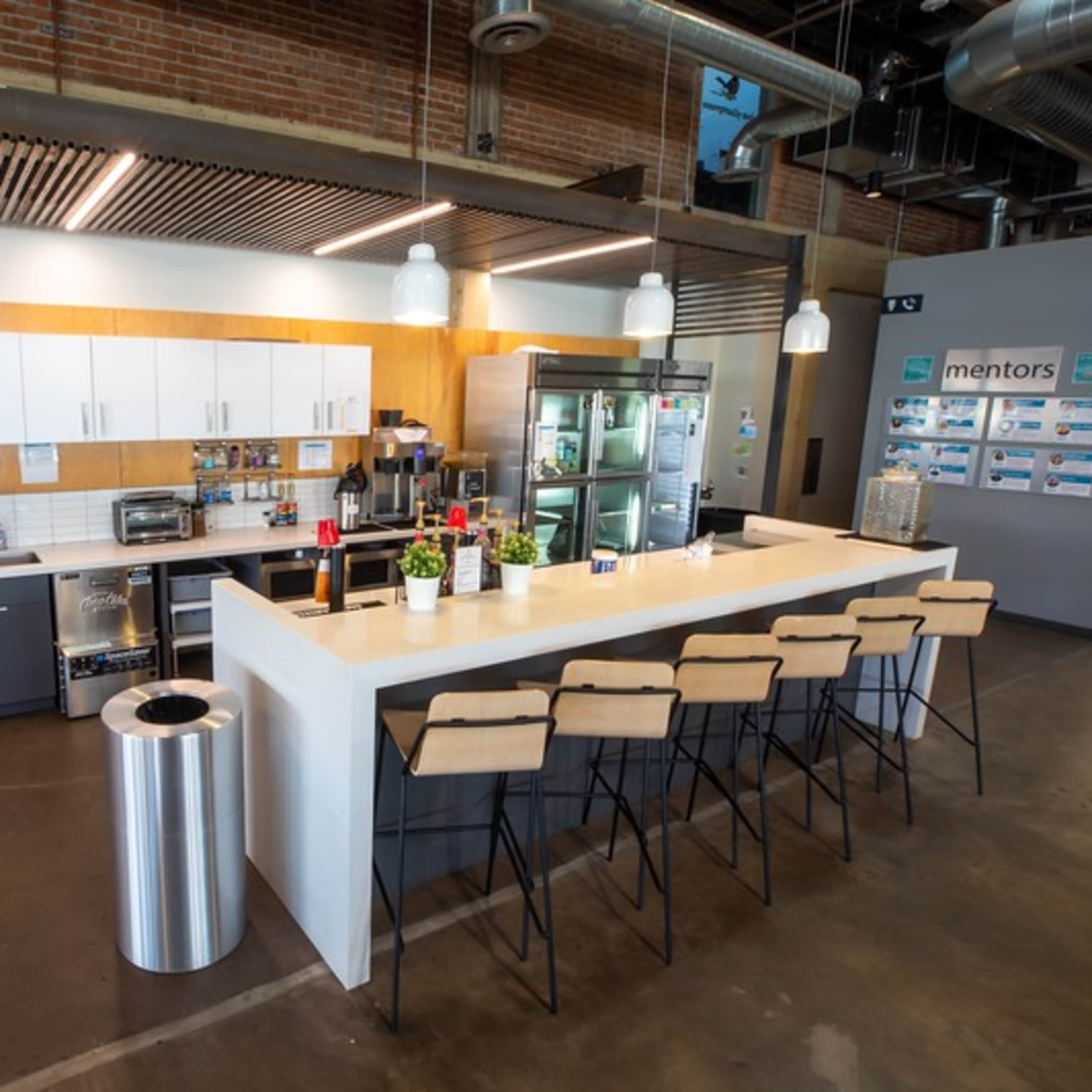 A modern kitchen area with a bar counter, seating, and various appliances, set against a backdrop of exposed brick and industrial-style decor.
