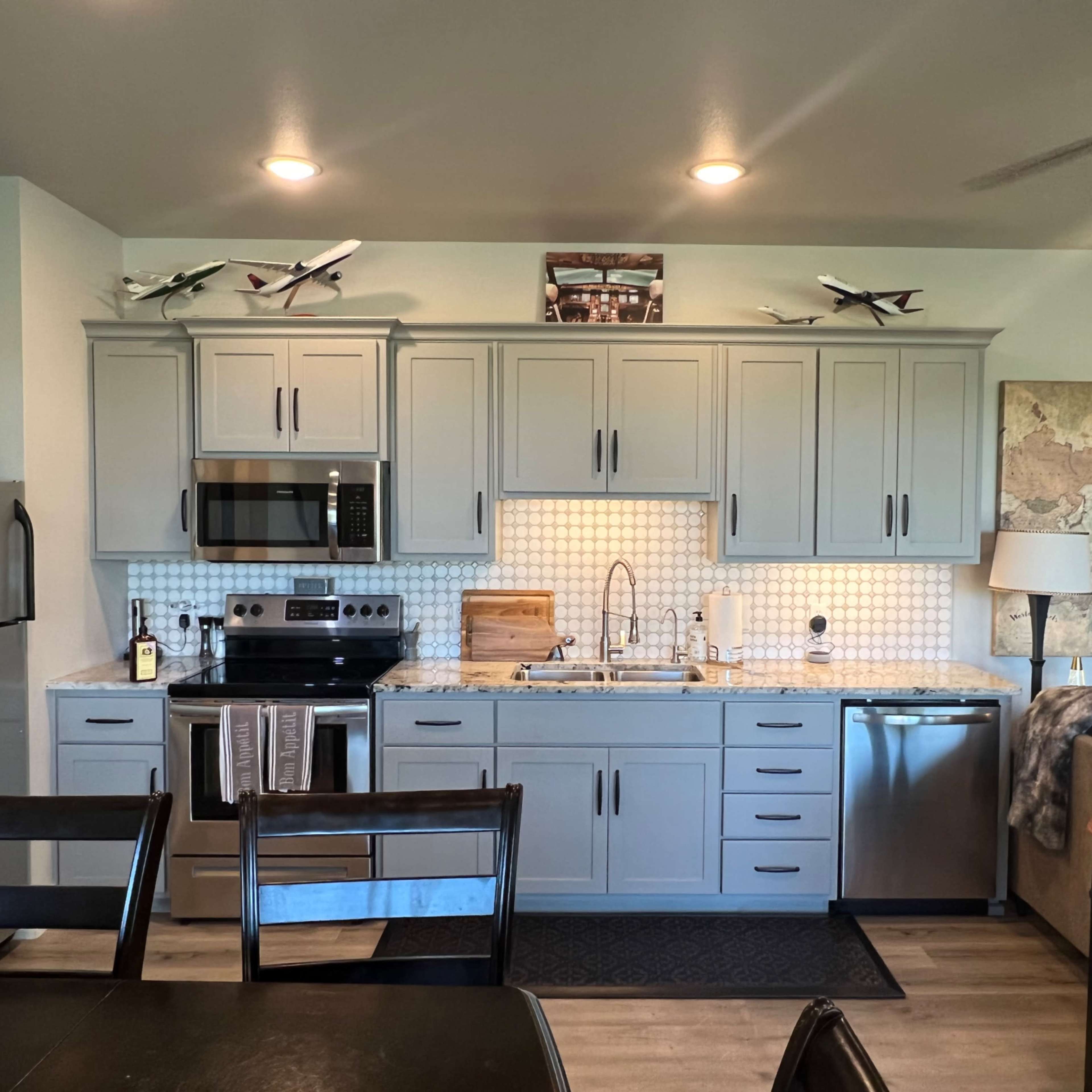 A modern kitchen features gray cabinets, stainless steel appliances, and a decorative map wall above the sink.