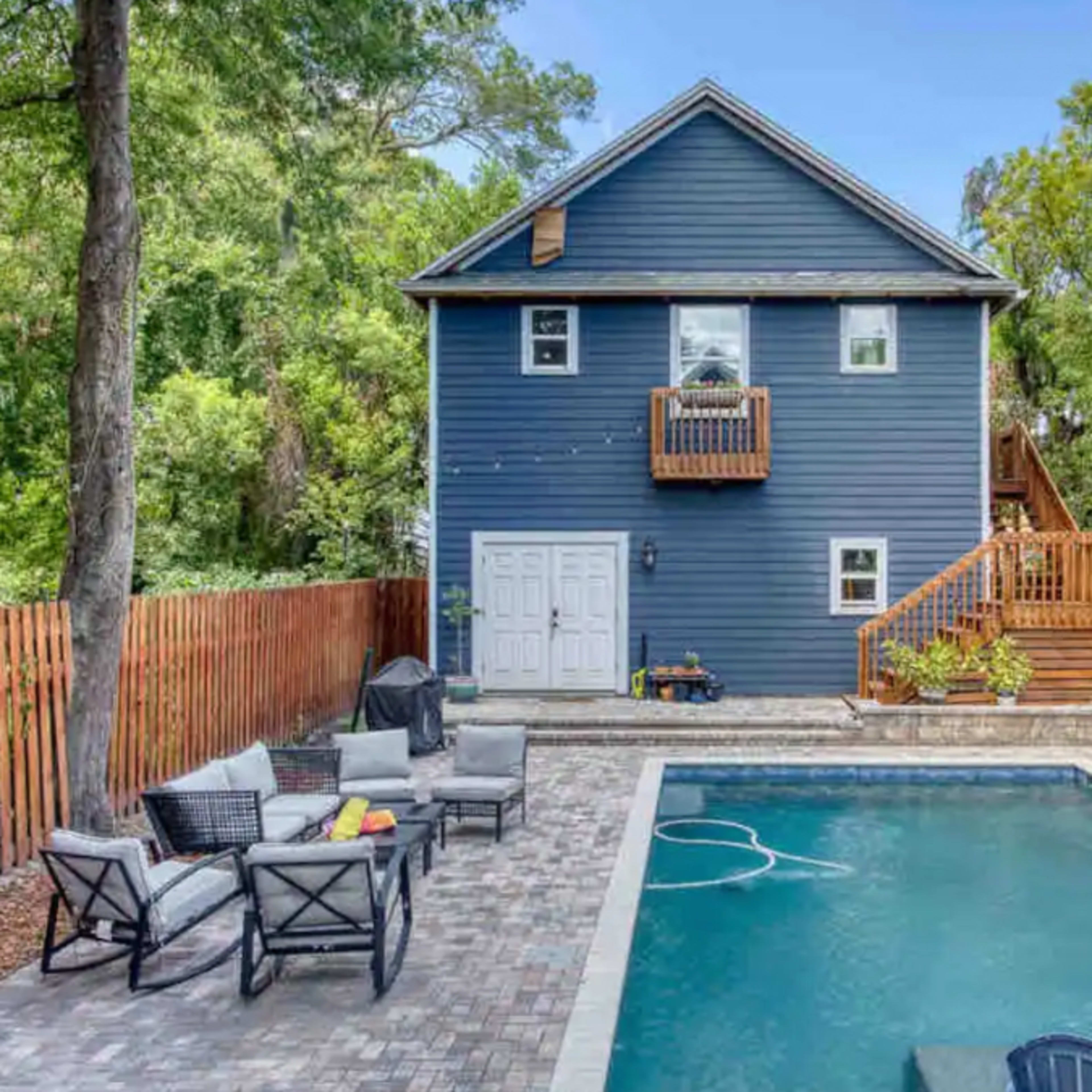A two-story blue house with a fenced backyard features a swimming pool and a patio area with seating.