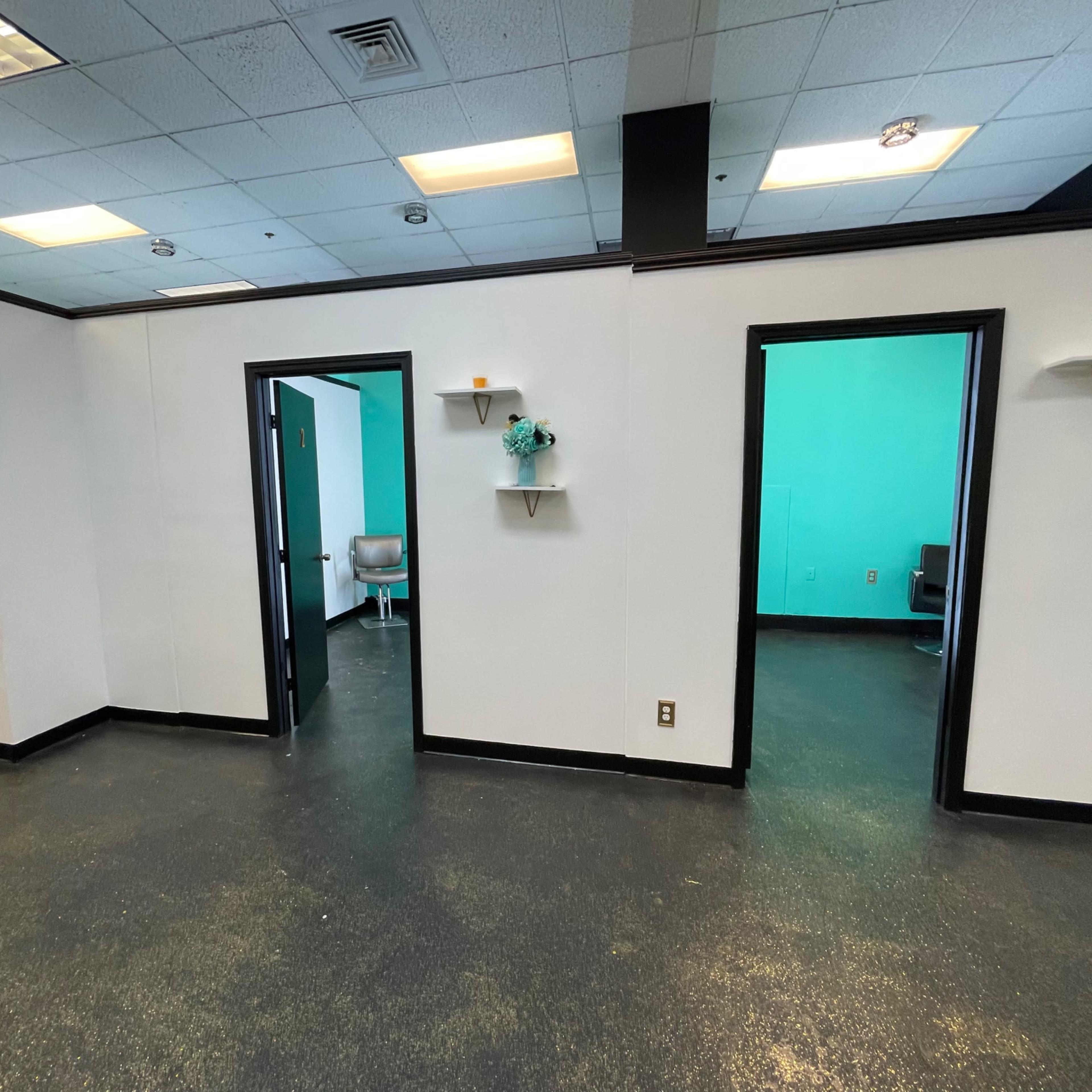 A spacious, well-lit interior with multiple doorways leading to rooms painted in a teal color, along with white walls and small shelves.