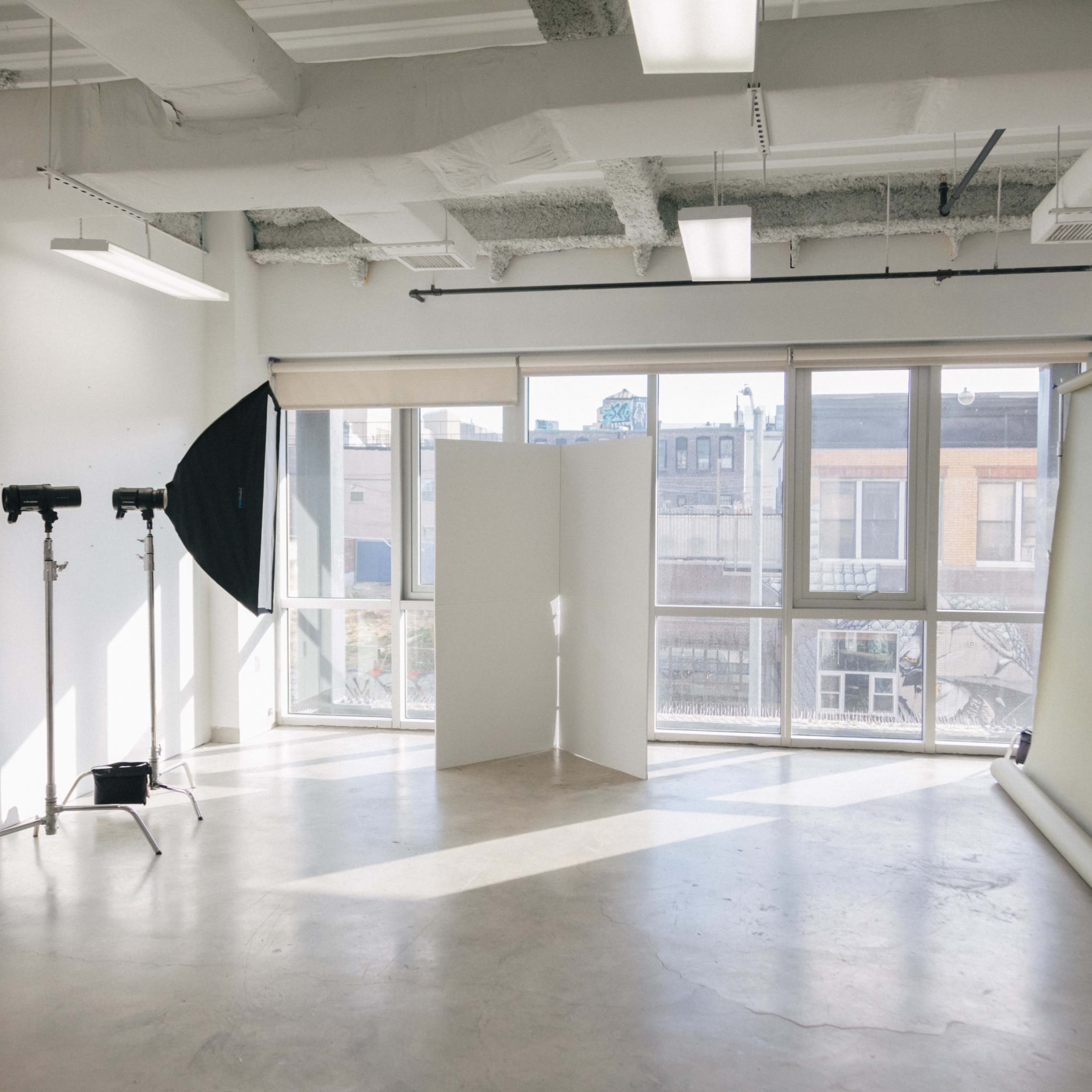 A well-lit photography studio with a backdrop, lighting equipment, and large windows overlooking a cityscape.