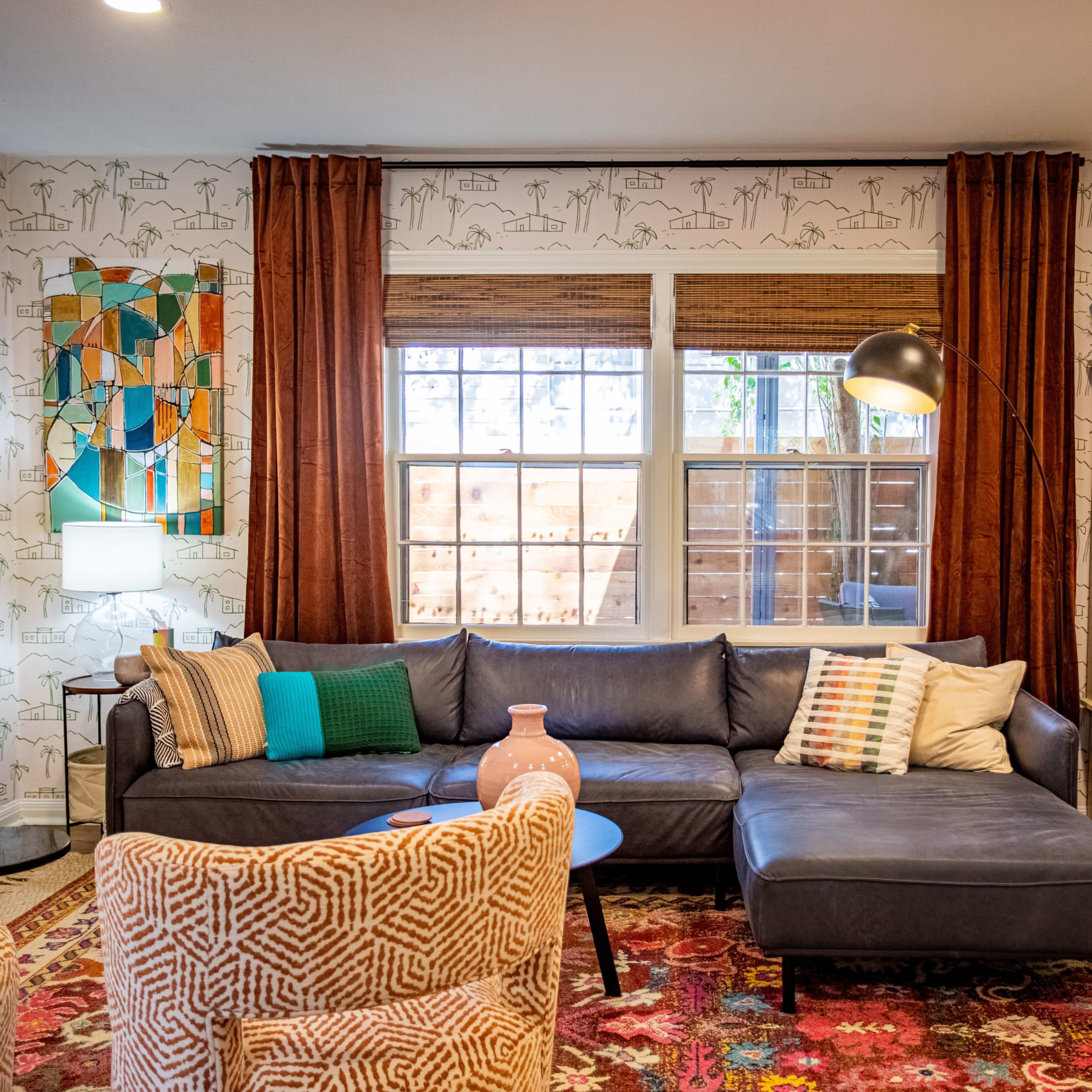 A cozy living room features a dark blue sectional sofa, patterned rugs, and decorative elements like a floor lamp, art on the walls, and a mix of colorful pillows.