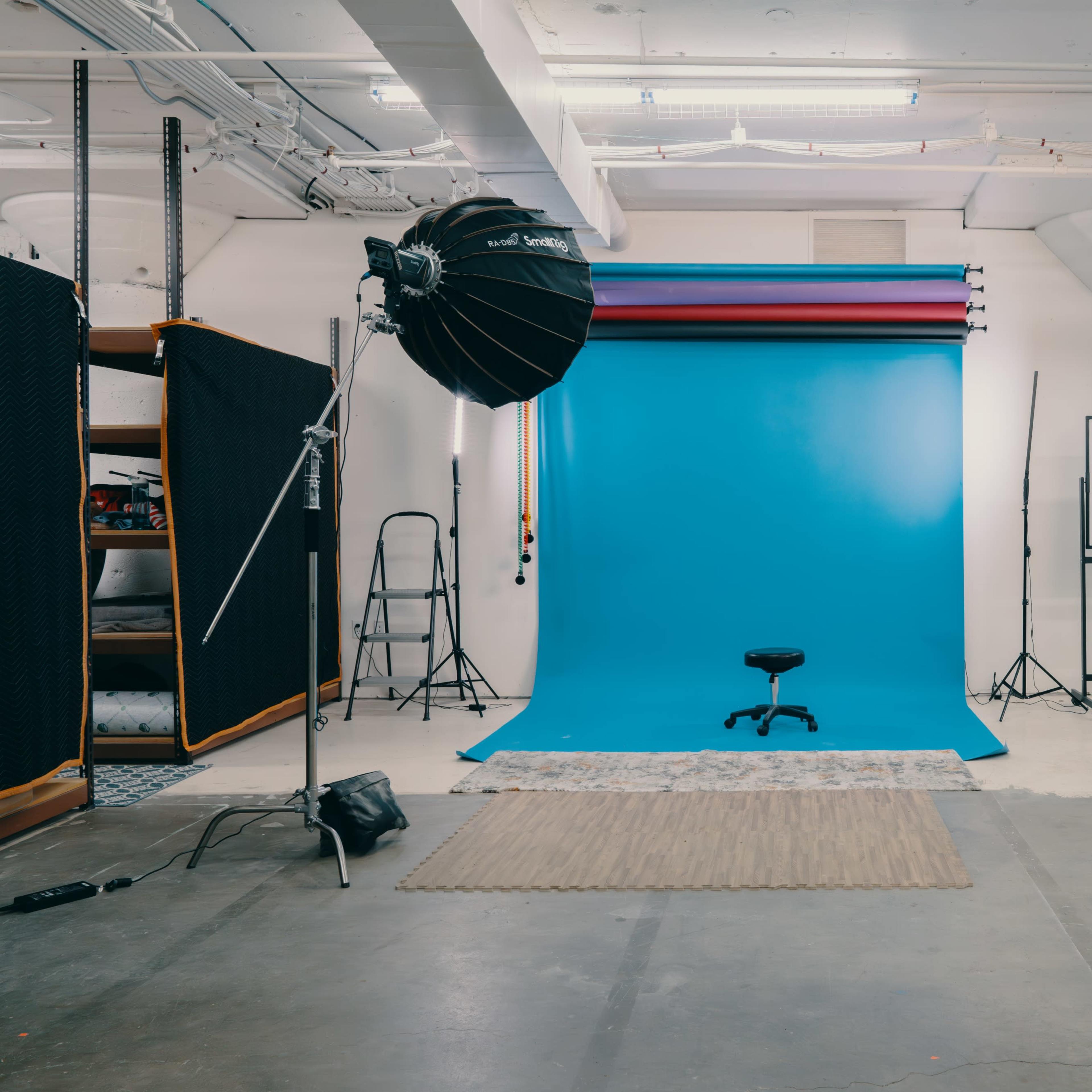 A photography studio with a blue backdrop, two softbox lights, and a stool positioned in front of the backdrop.