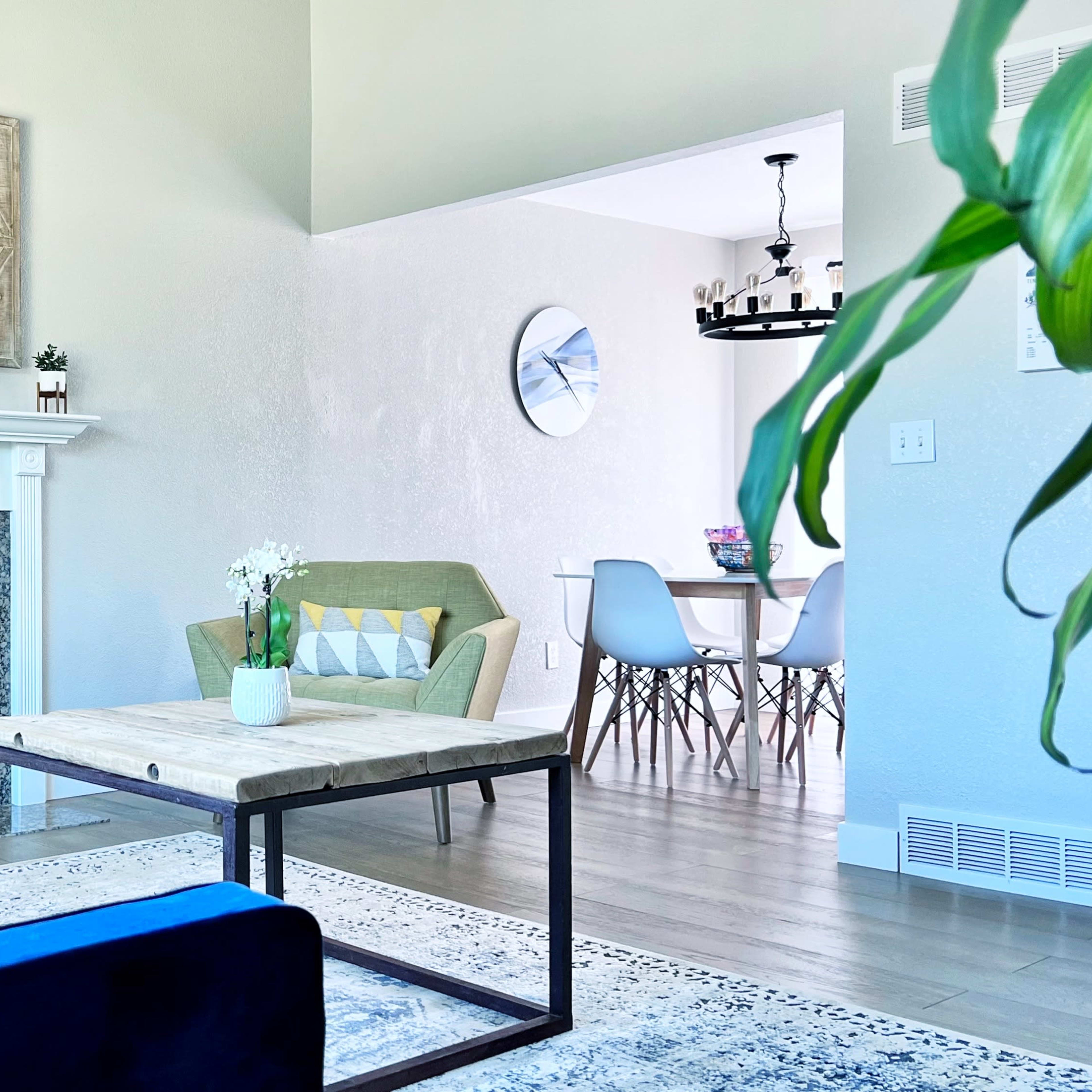 A bright living room features a blue couch, a beige armchair, a coffee table, and a fireplace surrounded by a decorative mantle.