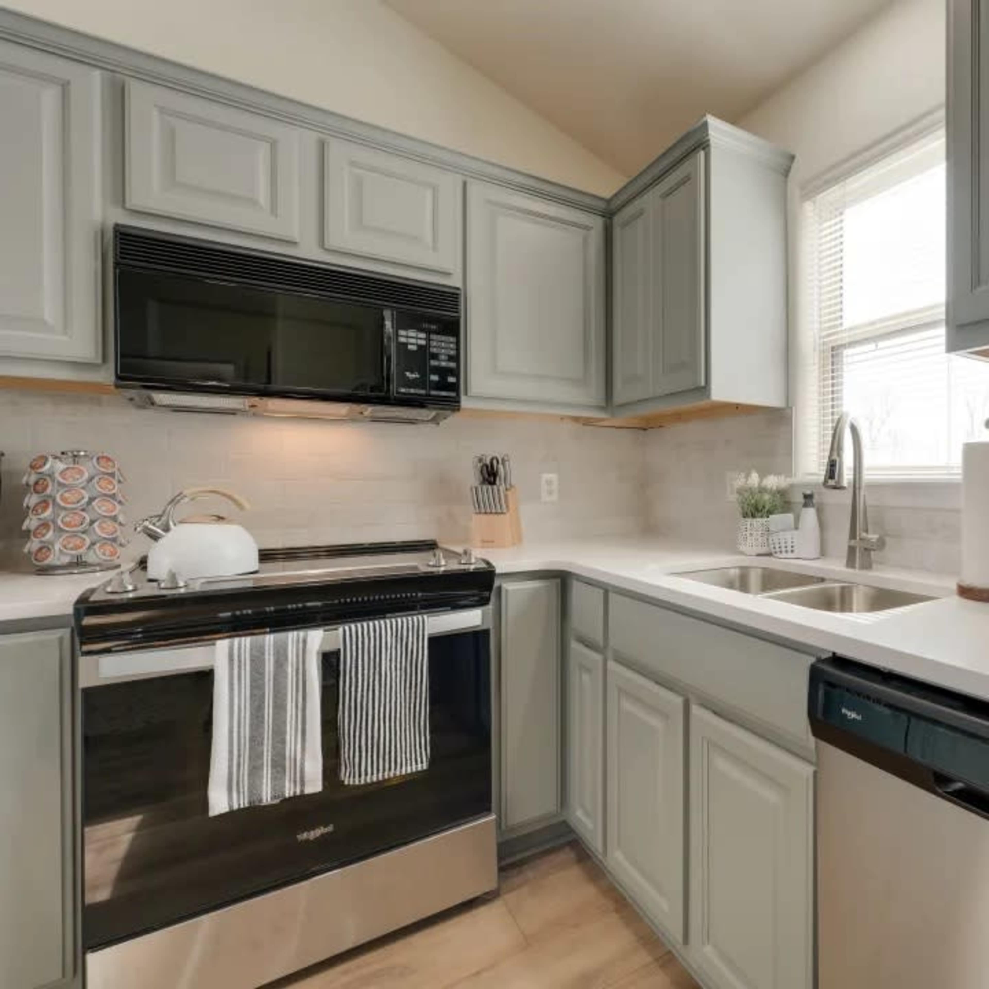 A kitchen with light gray cabinets, a black stove, a silver dishwasher, and a double sink under a window.