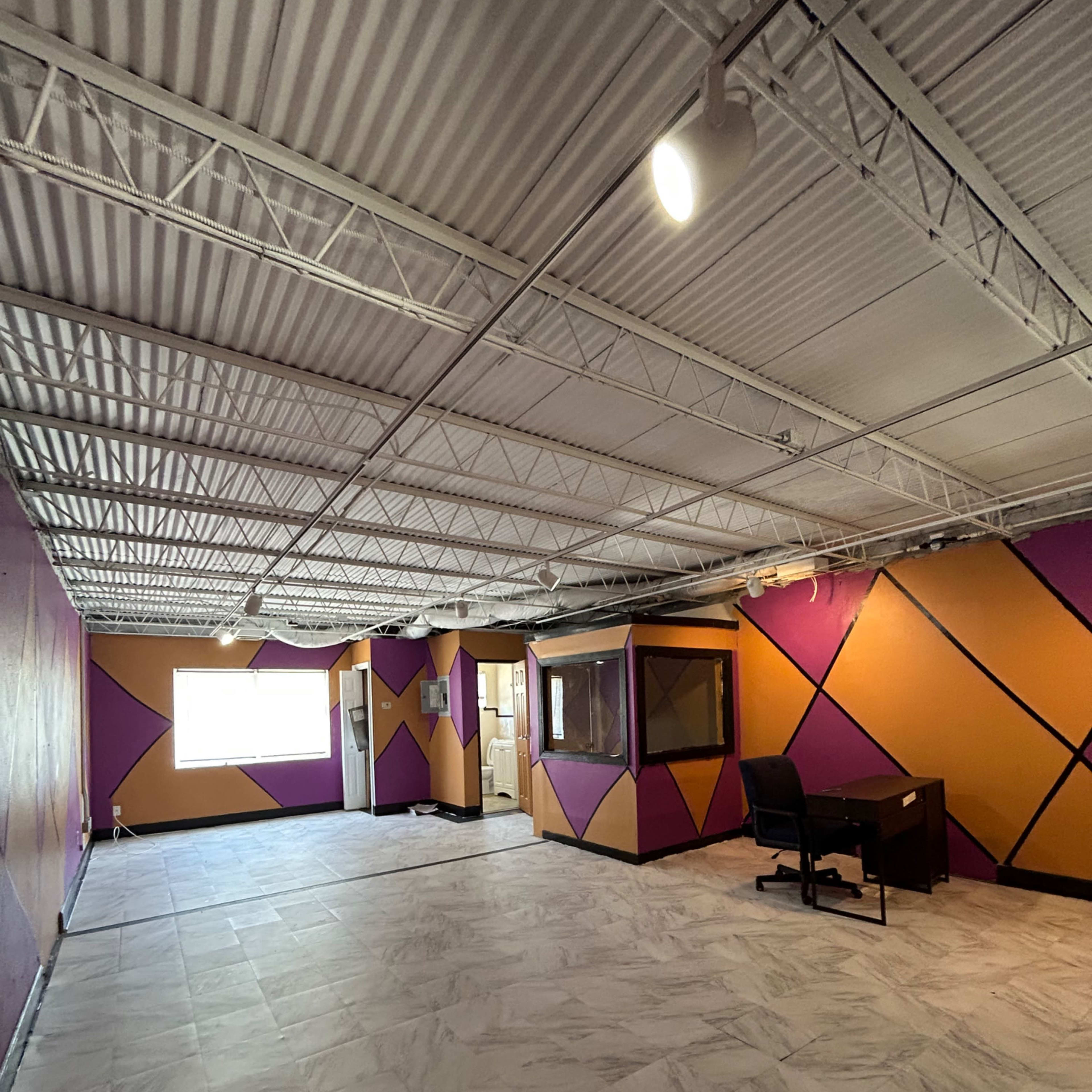 An empty room with purple and gold geometric wall patterns and a dark desk with a chair.