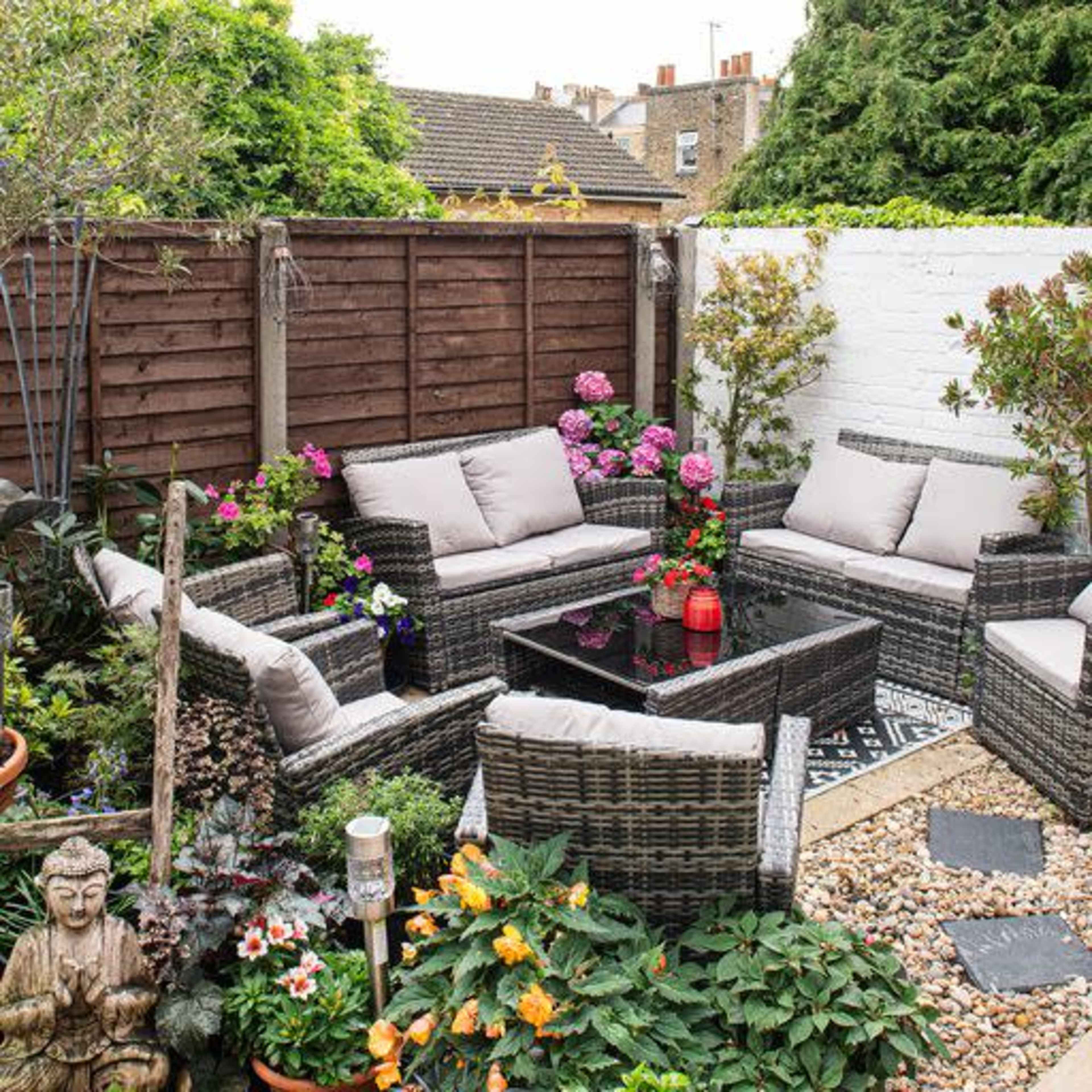 A well-decorated outdoor seating area surrounded by plants and flowers, featuring a wicker furniture set and a stone pathway.